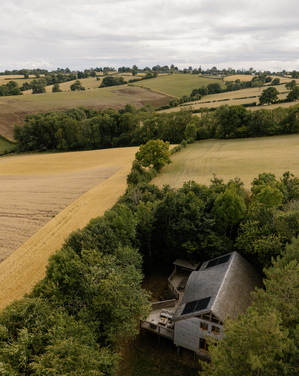 An aerial view of rolling farmland with fields, trees, and a house among the trees.
