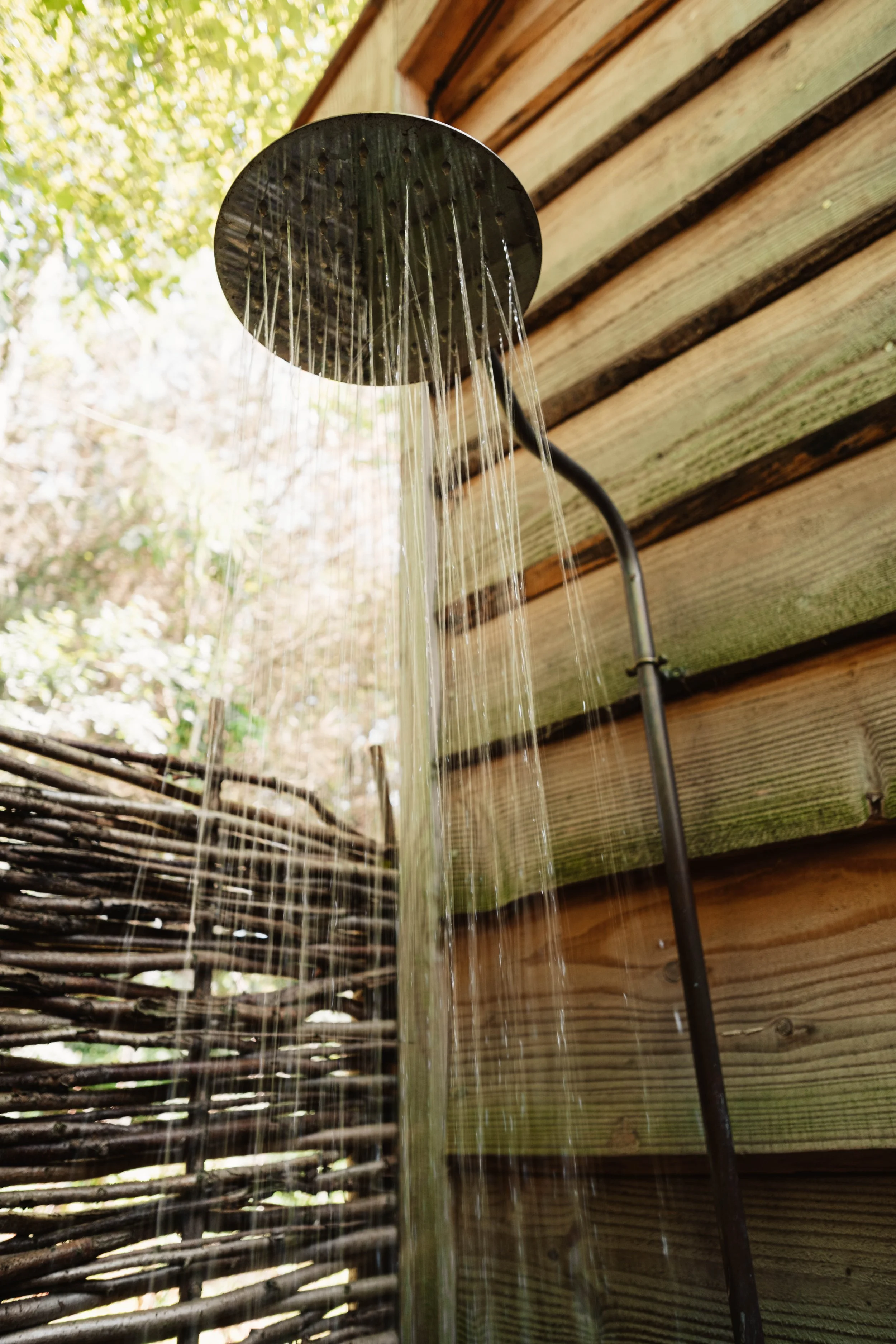 Private outdoor rainfall shower beside Journeyman Treehouse with rustic woven woodland screening