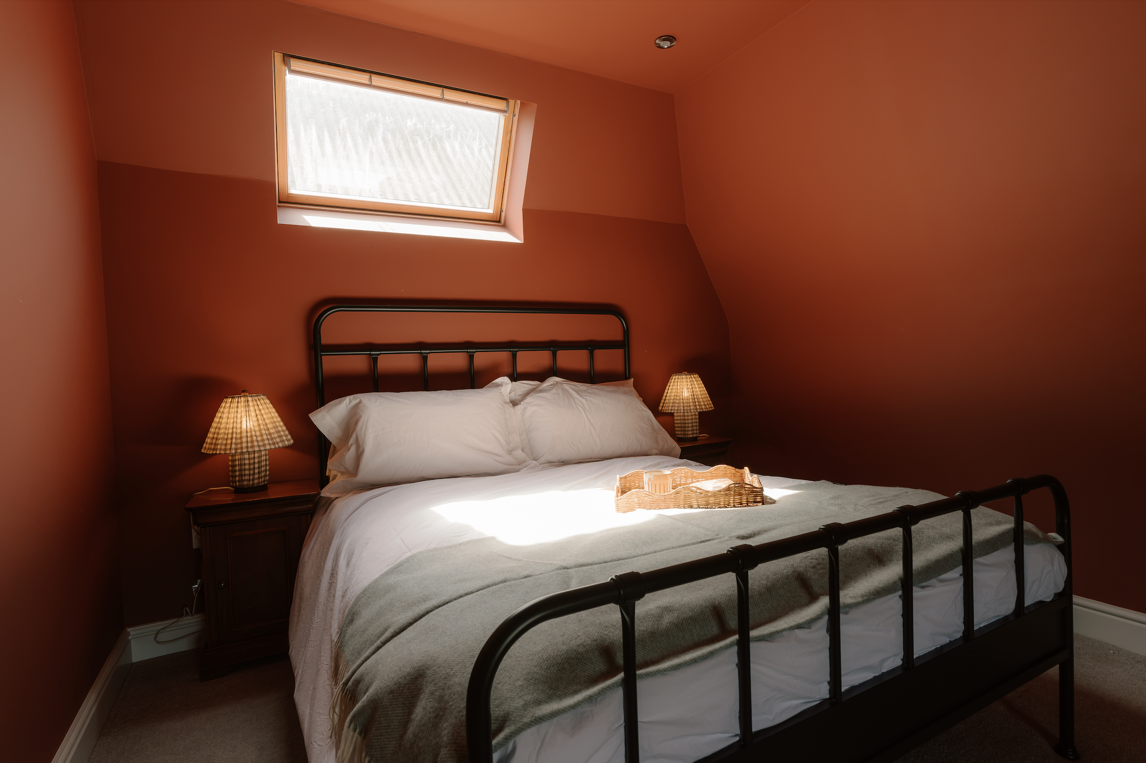 A bedroom with a bed, two nightstands with lamps, and a skylight window on the ceiling.