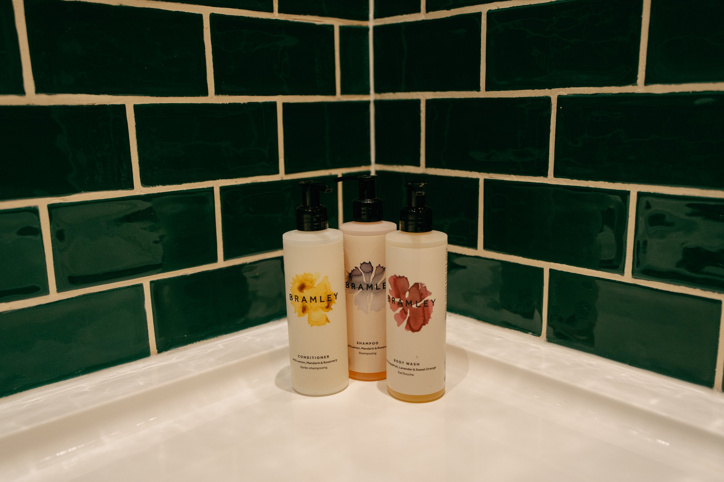 Three bottles of Bramley bath products on a white surface with dark green tiled wall background.