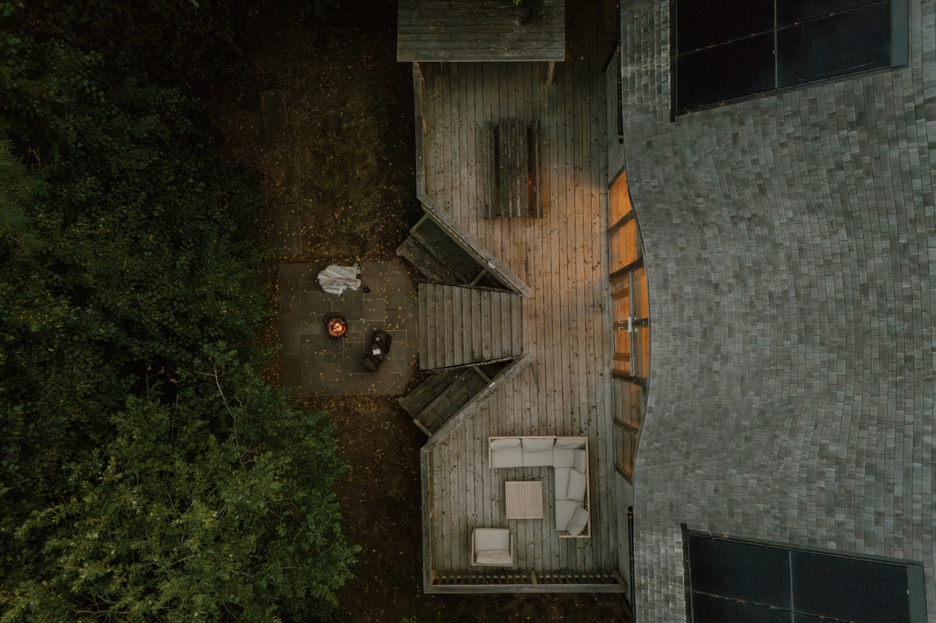 Aerial view of Journeyman Treehouse showing its large private deck, outdoor seating and fire pit surrounded by woodland