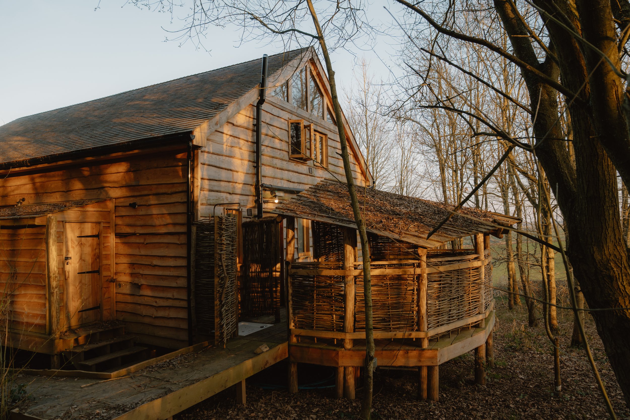 Rustic wooden cabin with woven exterior and trees in the background
