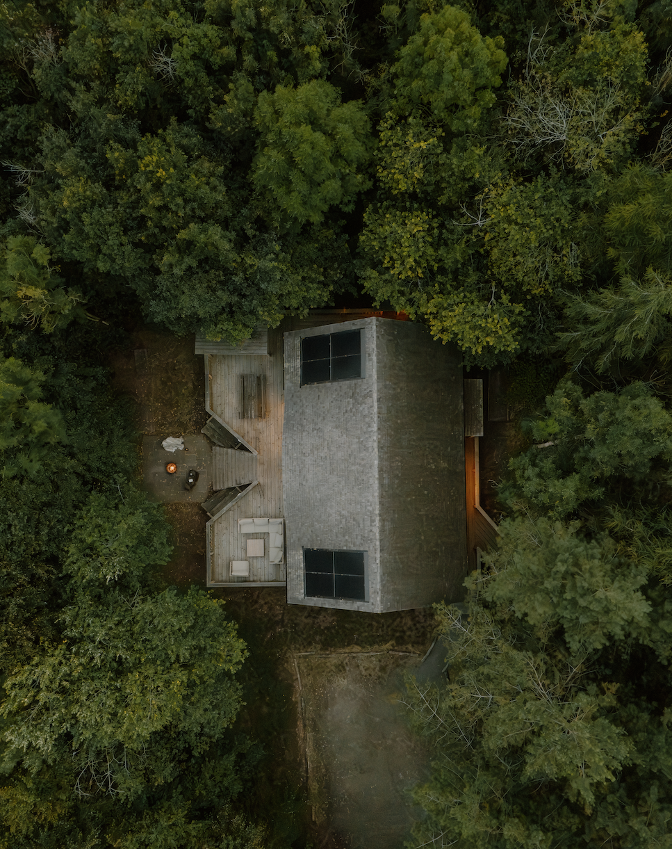 An aerial view of a house surrounded by dense green trees, with a deck and outdoor furniture visible.