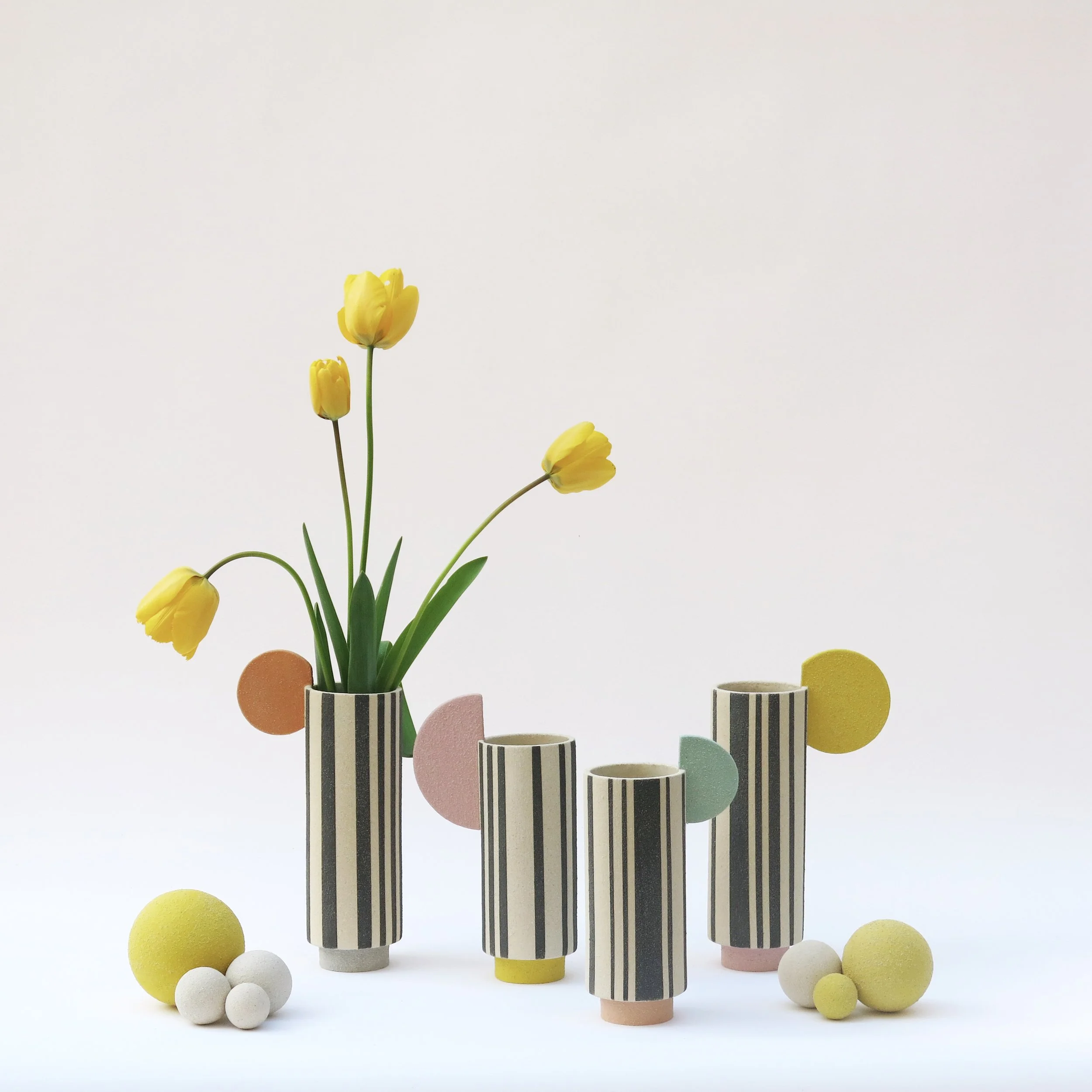 Vases Colonnes en grès chamotté décorés à l’engobe avec lignes noires et formes colorées, présentés avec tulipes jaunes, création Julie-Zoé Michel.
