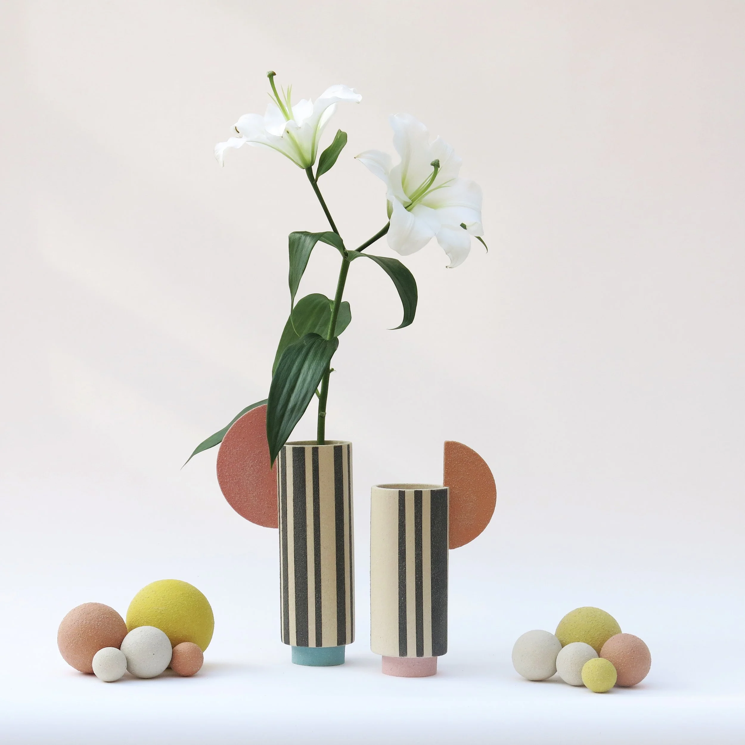 Deux vases Colonnes en grès chamotté décorés à l’engobe, lignes noires et forme colorée, présentés avec fleur blanche, Julie-Zoé Michel.