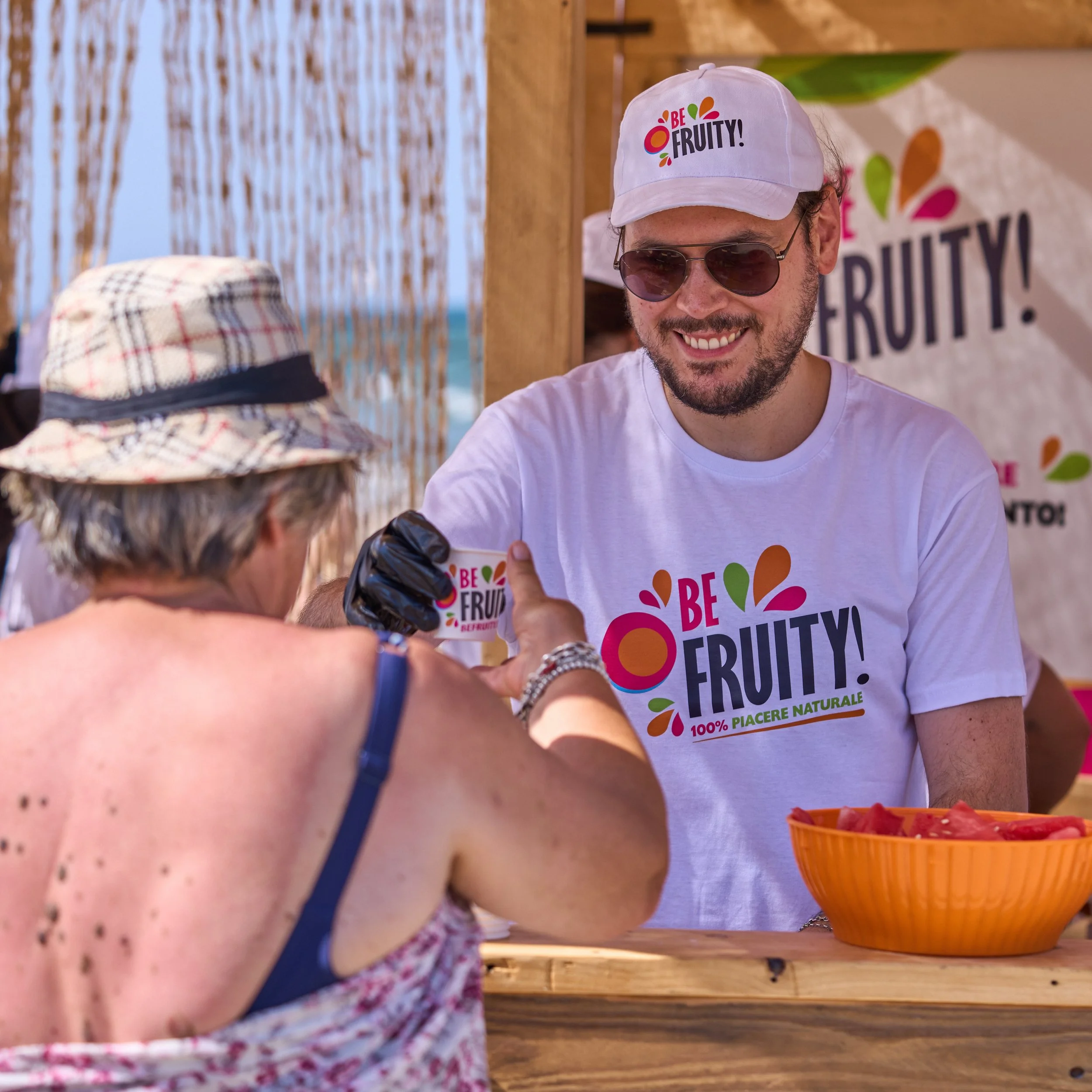 Staff handing out fresh fruit to beachgoers under umbrellas in Rimini
