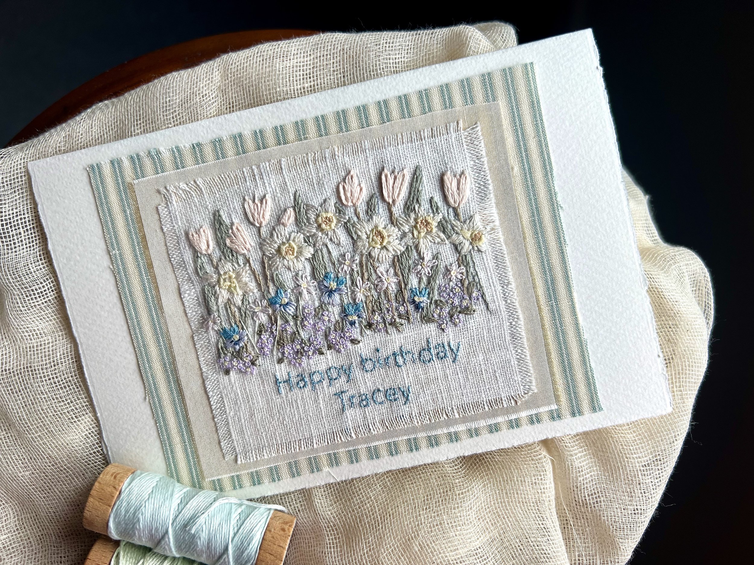 A handmade embroidered birthday greeting card with daffodils, pansies, daisies and other spring flowers and the message 'Happy Birthday Tracey'