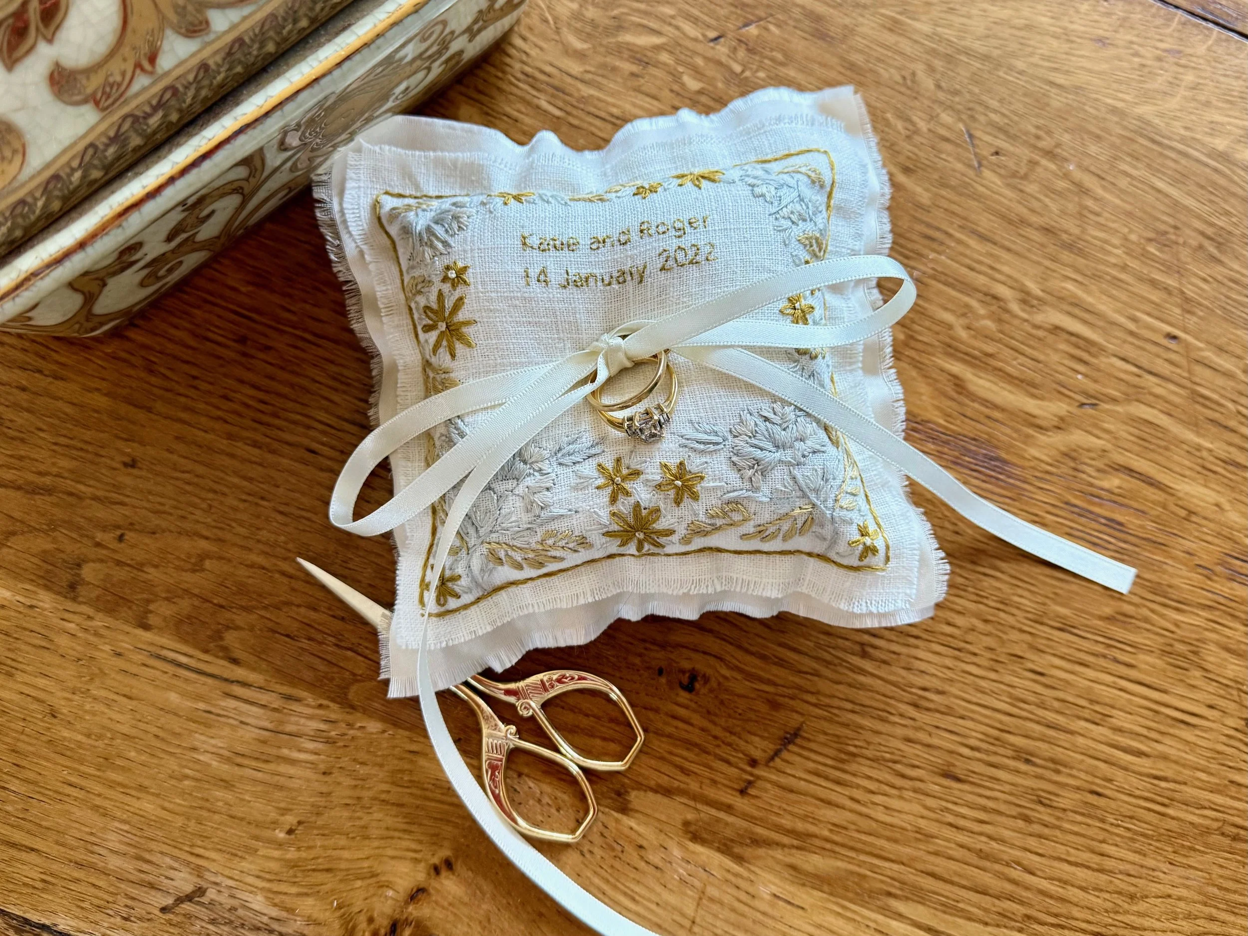 A hand embroidered wedding ring pillow with floral design a cream ribbon to tie the wedding rings; personalised with the wedding date and the names of the bride and groom.