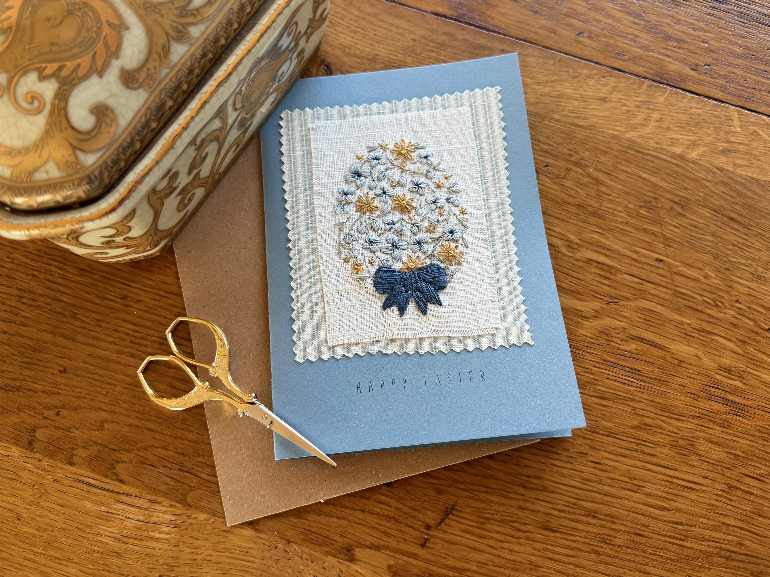 An Easter greeting card with hand embroidered floral Easter egg and blue bow.