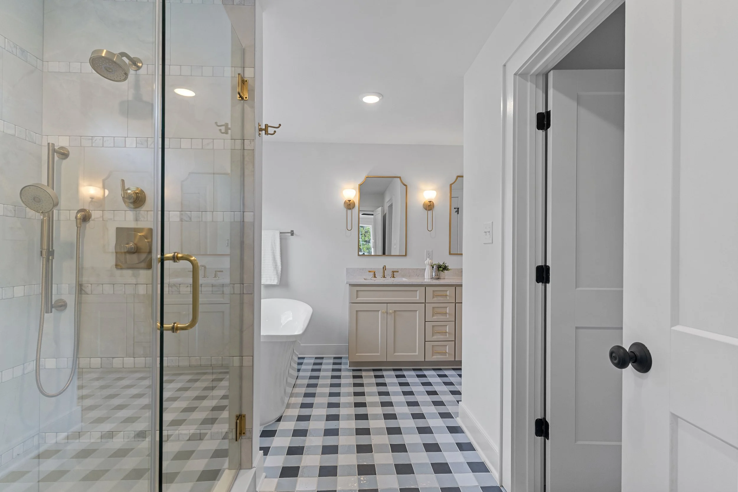 Bathroom with glass shower enclosure, beige vanity with gold fixtures, and black and white checkered floor tiles.