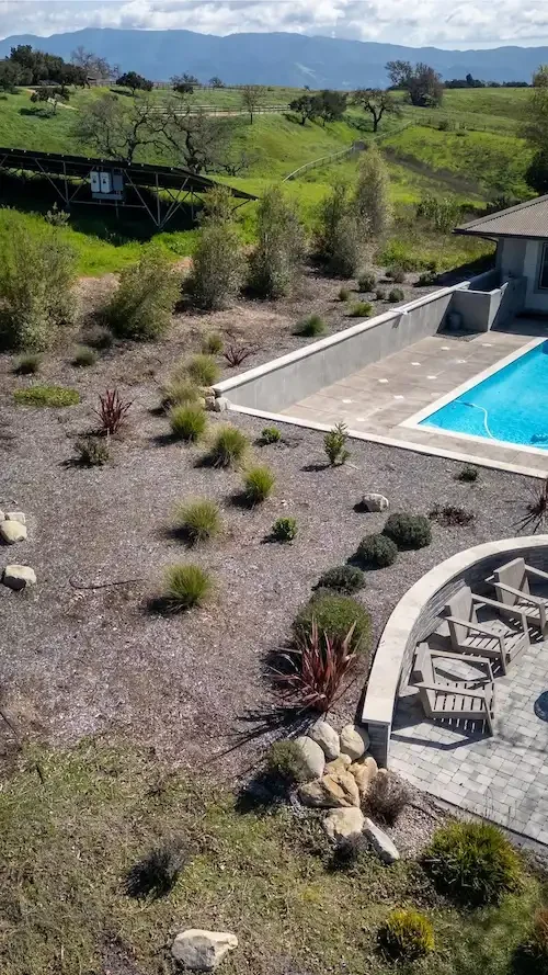 Aerial portrait view of a pool surround, curved fire pit patio, and drought-tolerant landscape design with Santa Barbara Valley hills in the background, by Legacy Landscape & Arboriculture