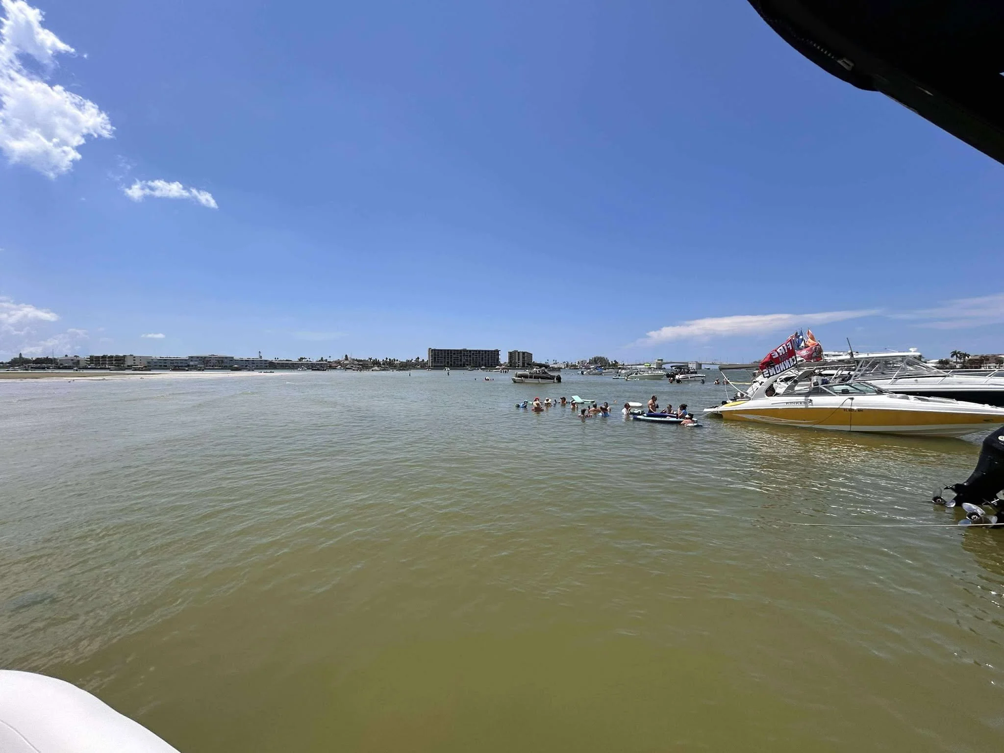 A group of people swimming and floating in the water near a dock with boats, under a clear blue sky.