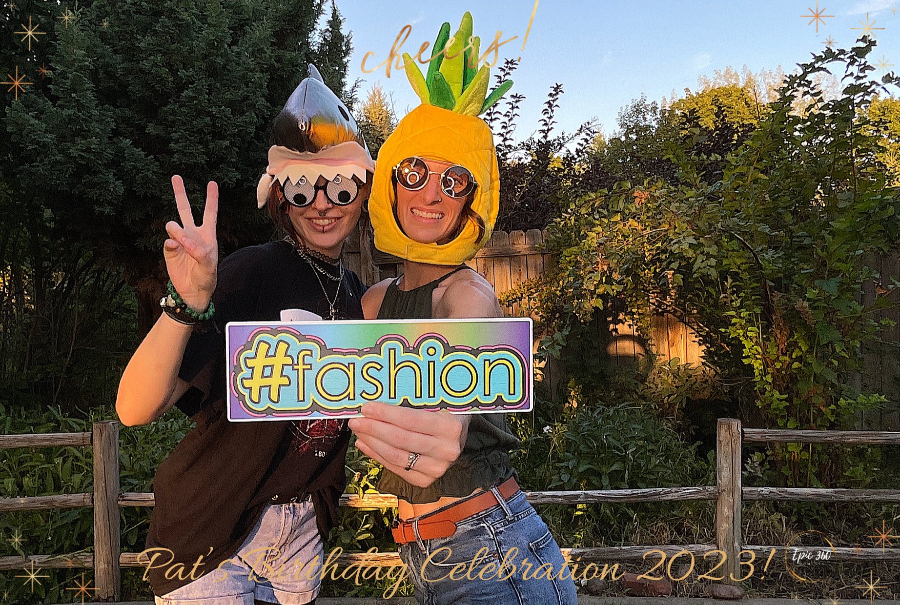 Two women smiling outdoors, wearing playful headgear resembling a shark and a pineapple, holding a sign that says '#fashion', and making peace signs. The photo is decorated with text celebrating a birthday celebration.
