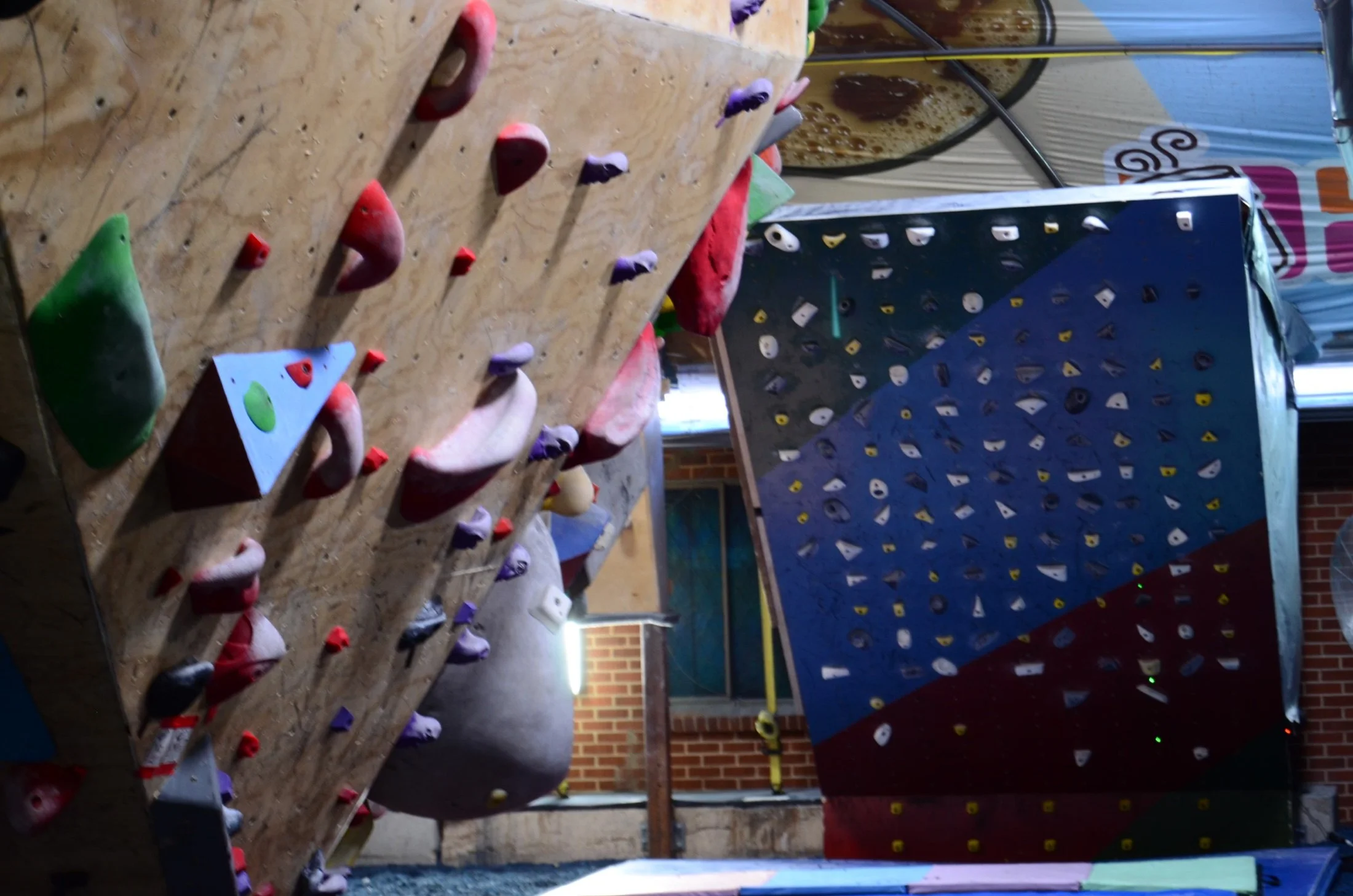 Indoor bouldering gym with various climbing holds on wooden walls and padded flooring.