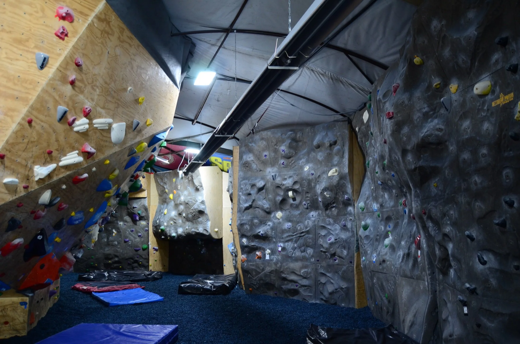 Indoor rock climbing gym with various climbing walls and colorful holds, padded flooring, and climbing pads.