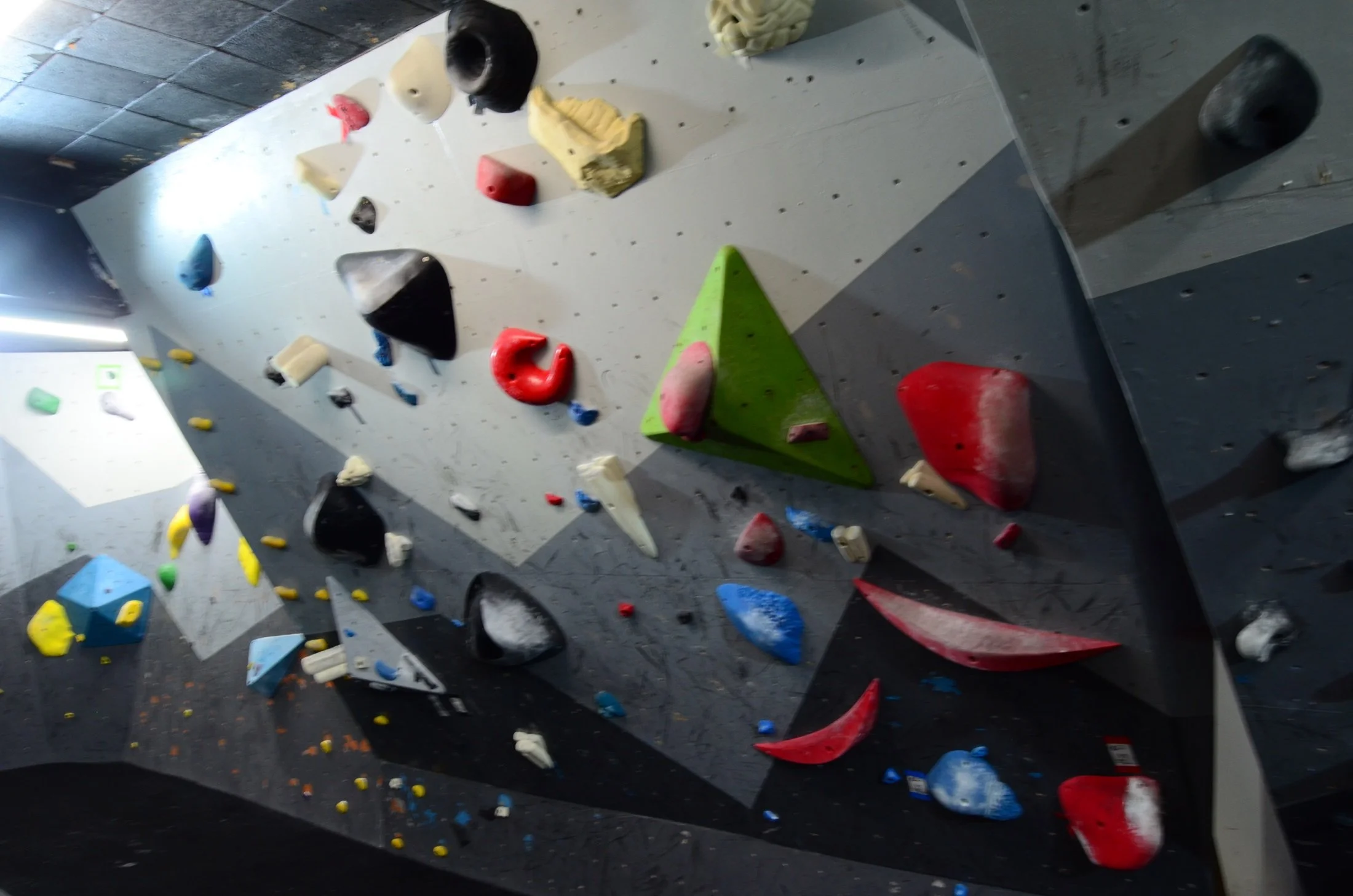 Indoor bouldering gym wall with various colorful climbing holds and voluminous holds attached to the wall for rock climbing practice.