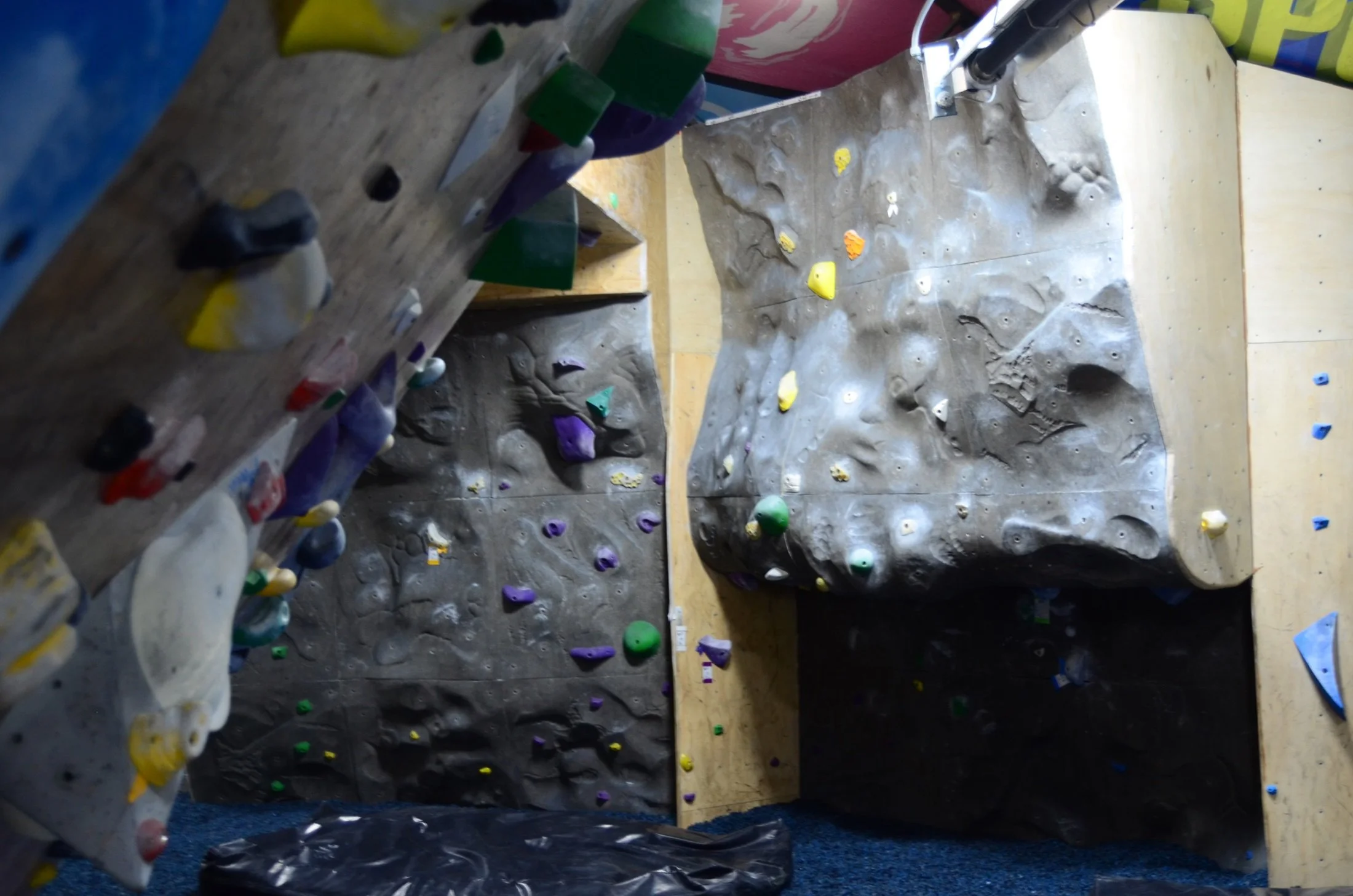 Indoor rock climbing gym with various climbing holds on textured walls and a blue padded floor.