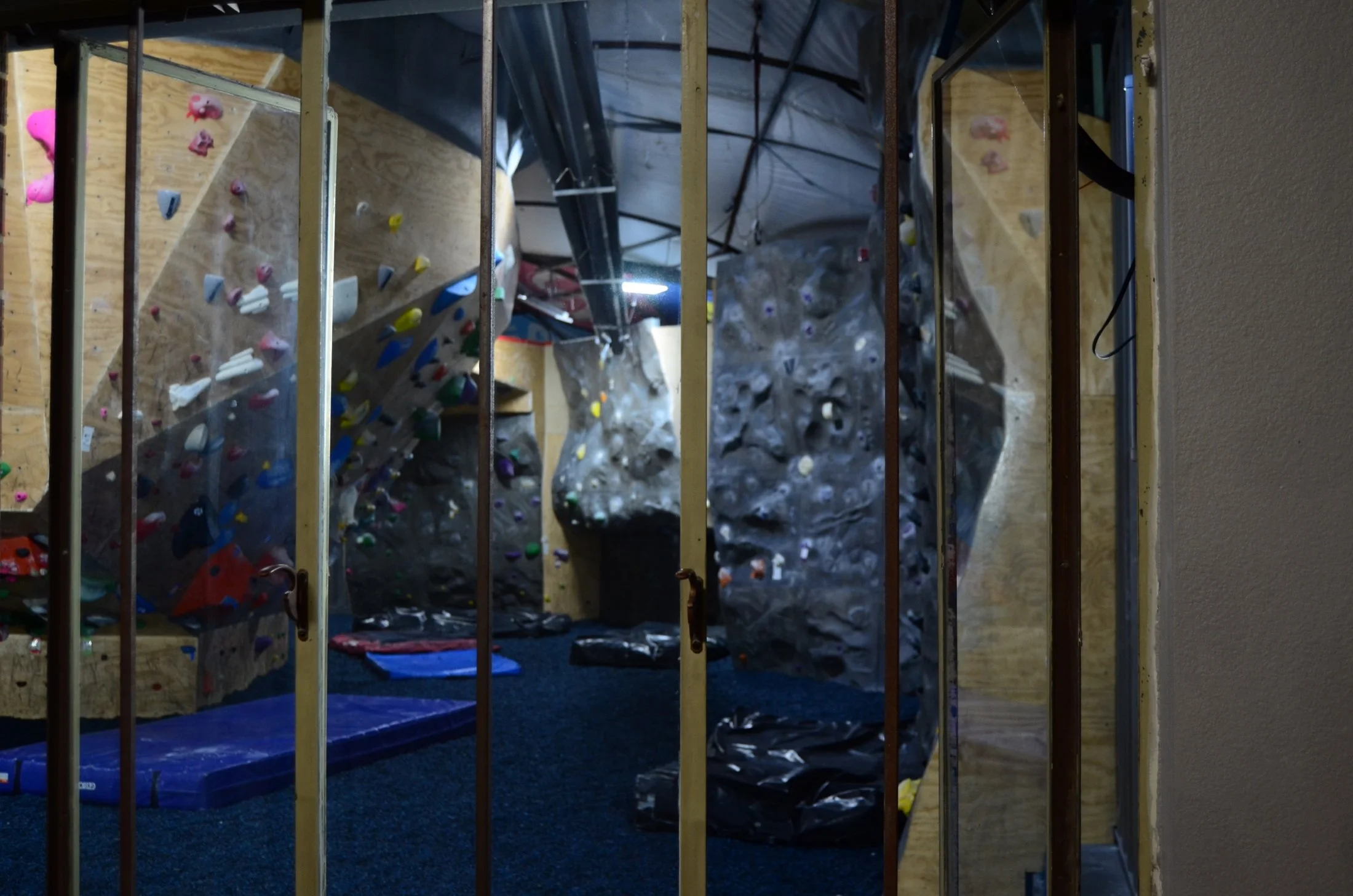 Indoor climbing gym with rocks and has climbing walls and holds, viewed through metal bars.
