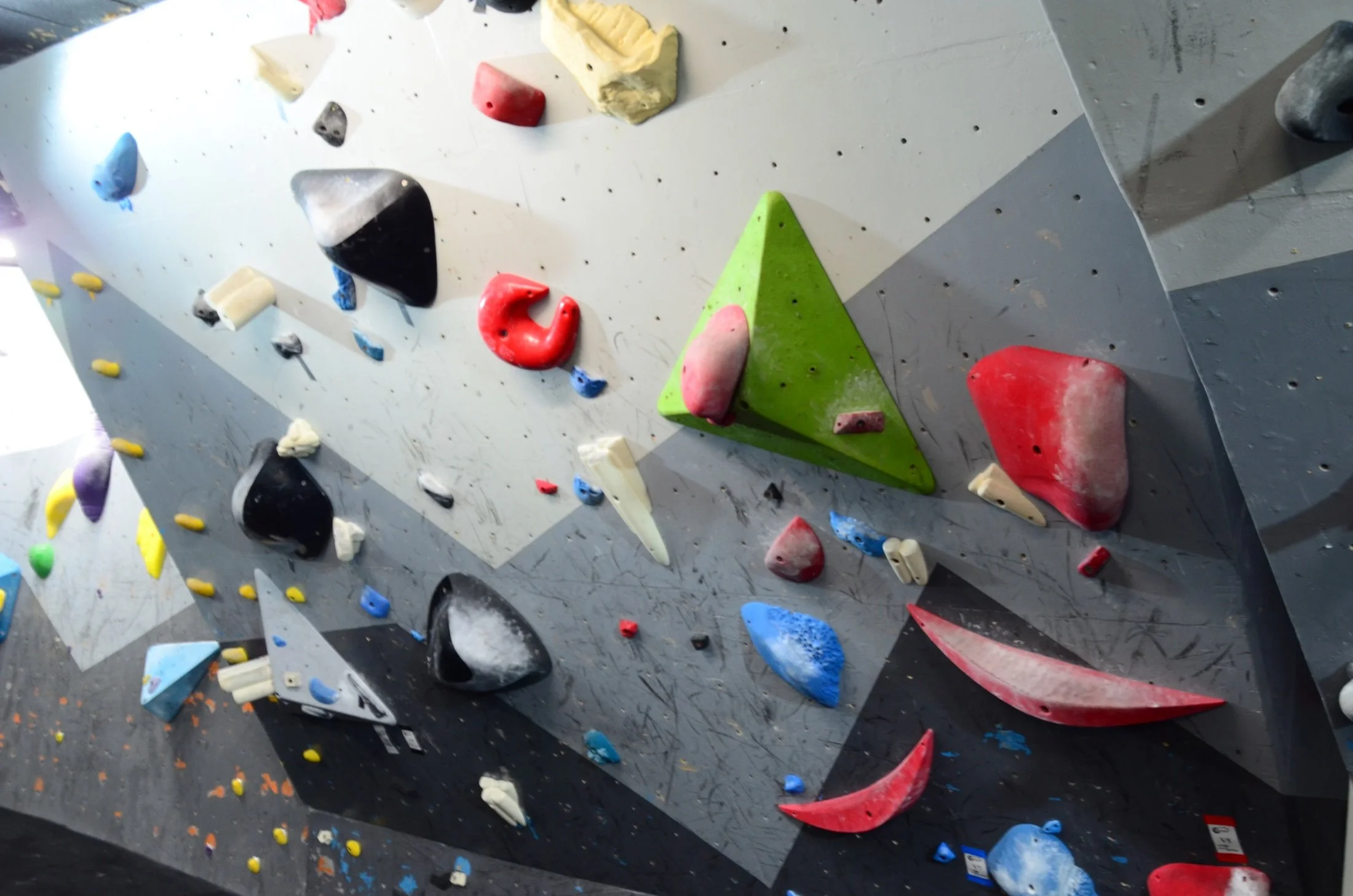 Indoor rock climbing wall with various colorful holds, including red, yellow, black, white, green, purple, and blue, attached to a gray surface.