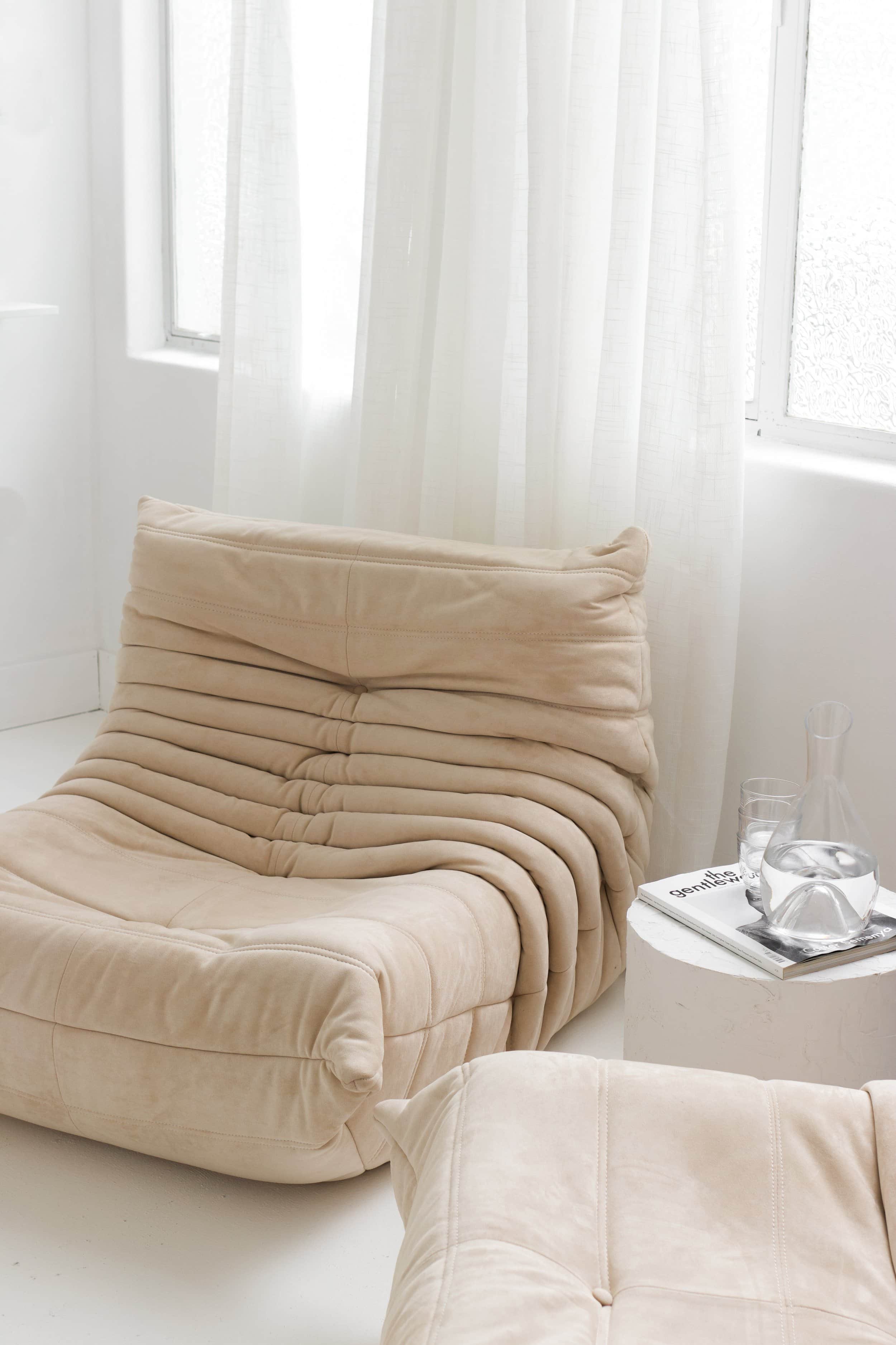 Neutral-toned modern lounge chair and side table in a minimalist interior space.