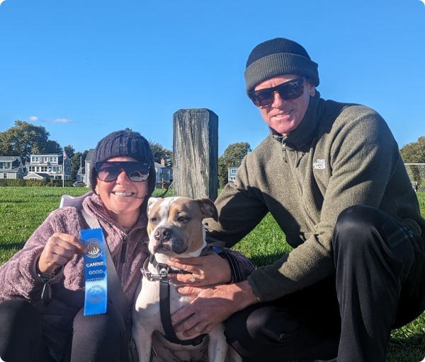 Two pet owners are smiling with their dog, who just earned a Canine Good Citizen Certification