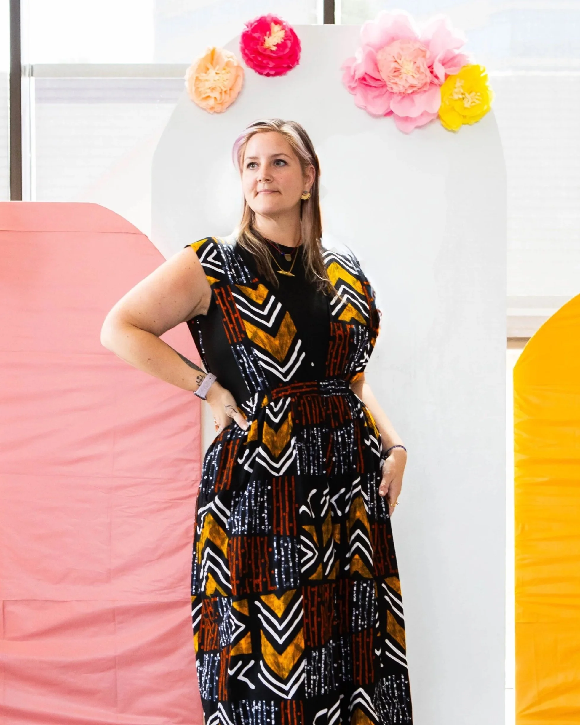 Woman in a colorful geometric patterned dress standing in front of large paper flowers and paper lanterns.