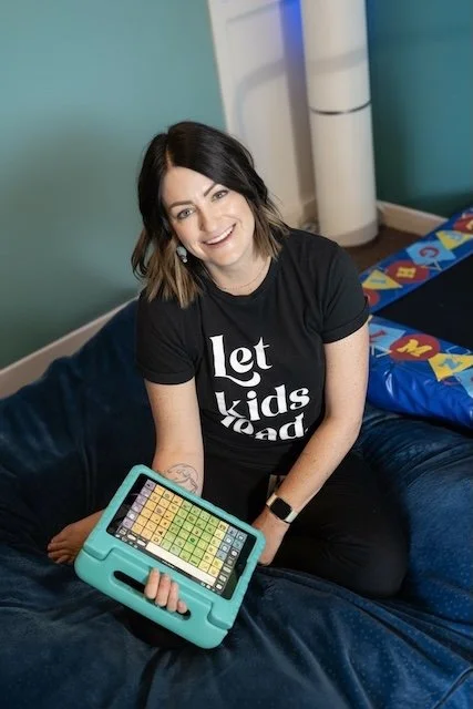 speech therapist sitting down holding and AAC device and smiling
