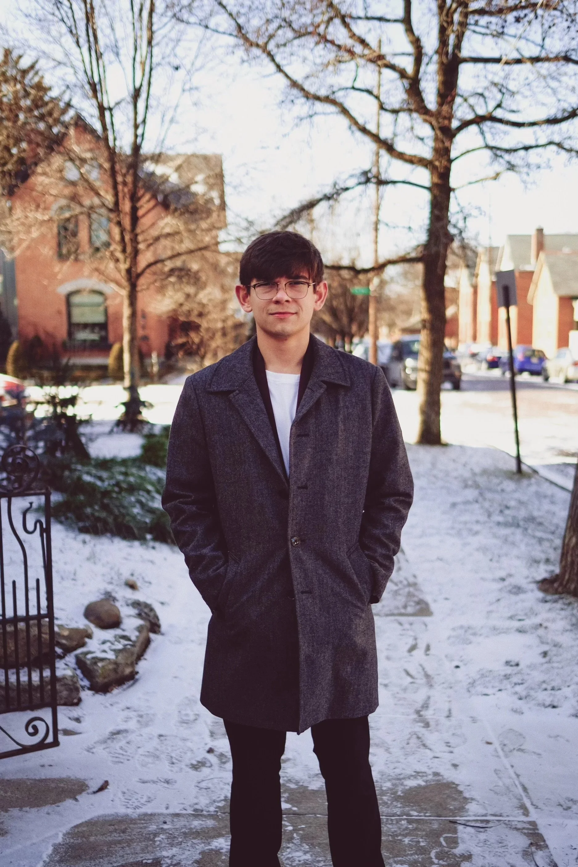 Young man in a gray coat standing outside on a snowy sidewalk.