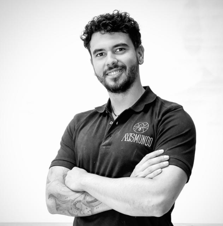 Krachtige portretfoto van een jonge man met getextureerd haar en een lichte baard, lachend met armen over elkaar, in zwart-wit, wijst naar professionaliteit en vertrouwen, draagt een polo met het logo 'AXIS-MUNDO'.