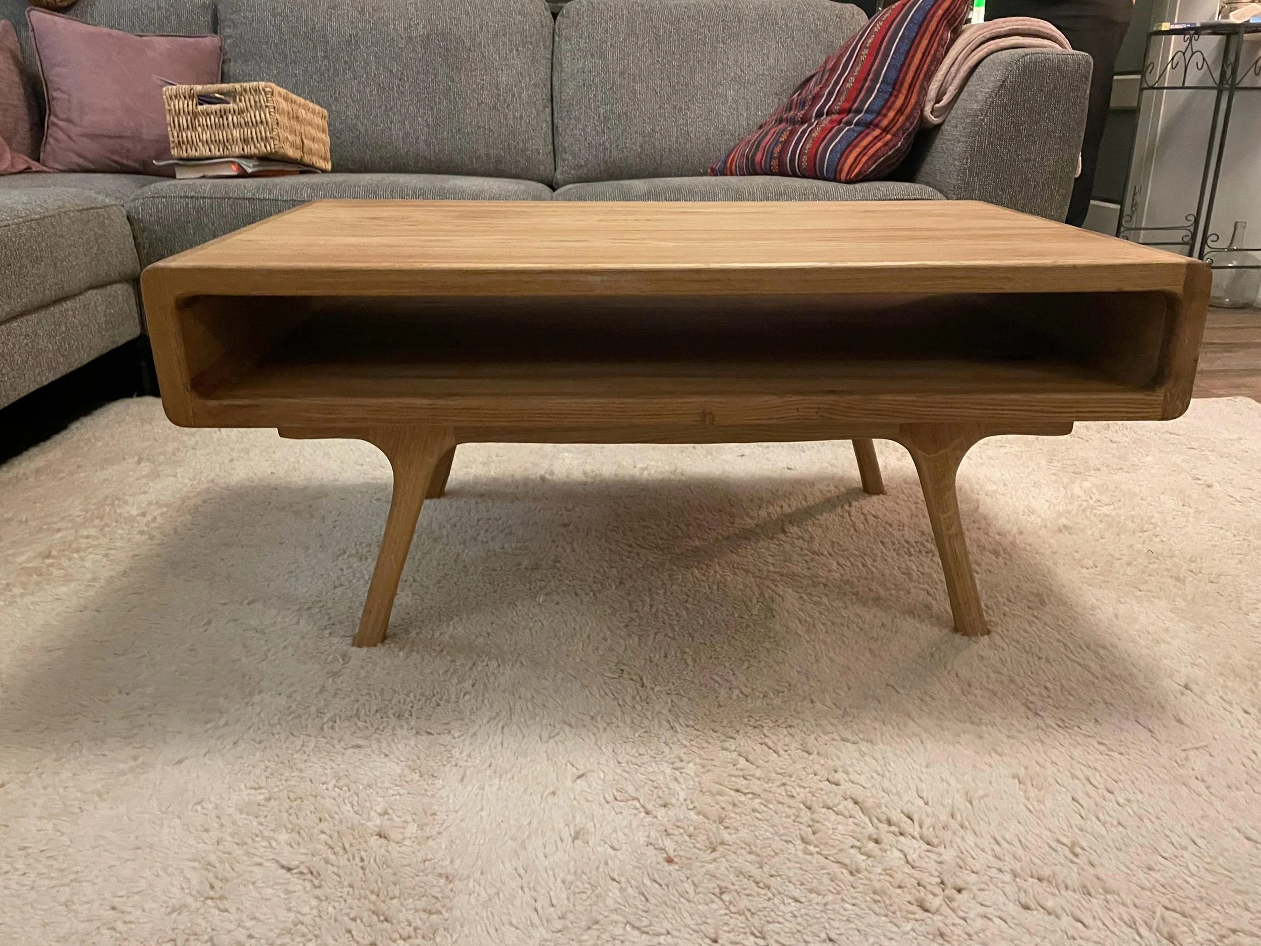 Houten salontafel in een woonkamer met een beige tapijt, een bank met kussens en een paar dekens op de achtergrond.