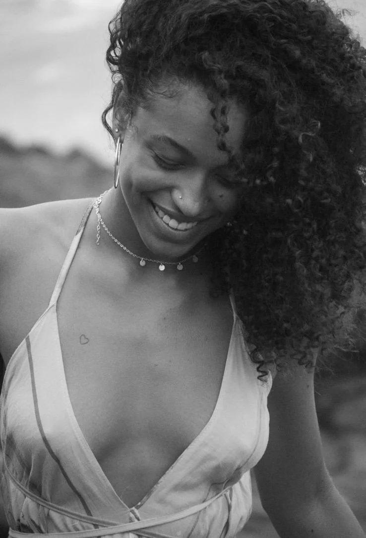 A smiling woman with curly hair modelling for a brand.