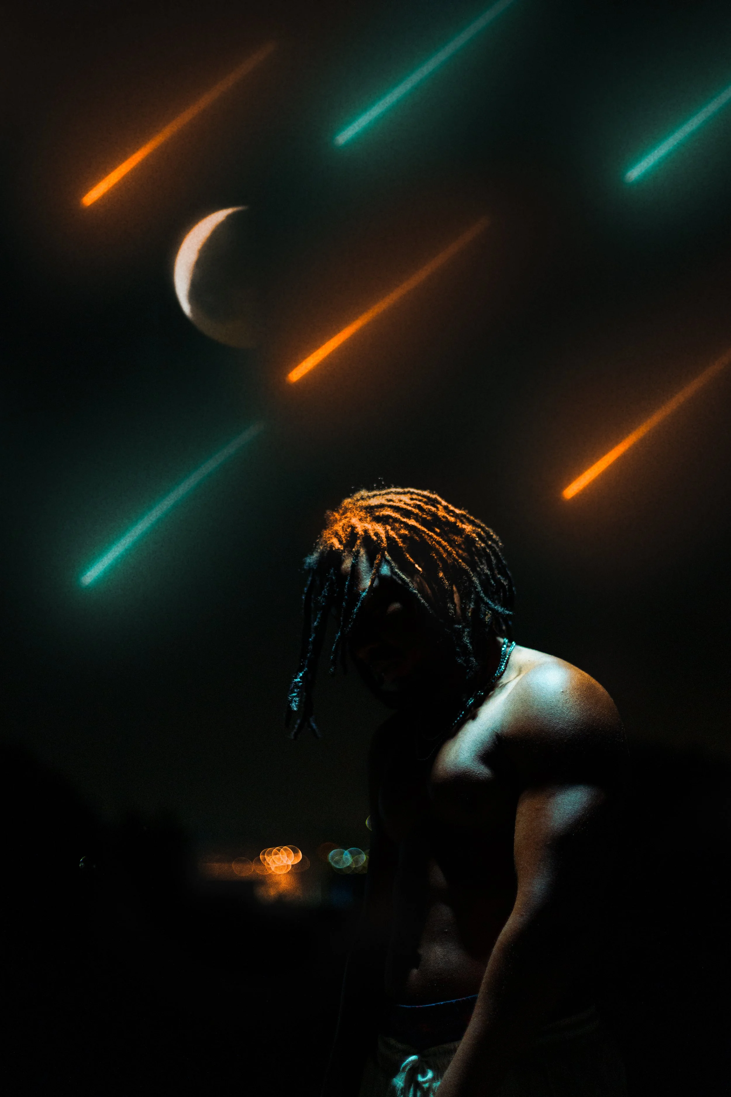 A shirtless person with dreadlocks is in the foreground, partially illuminated, against a dark background with colorful streaks and a crescent moon.