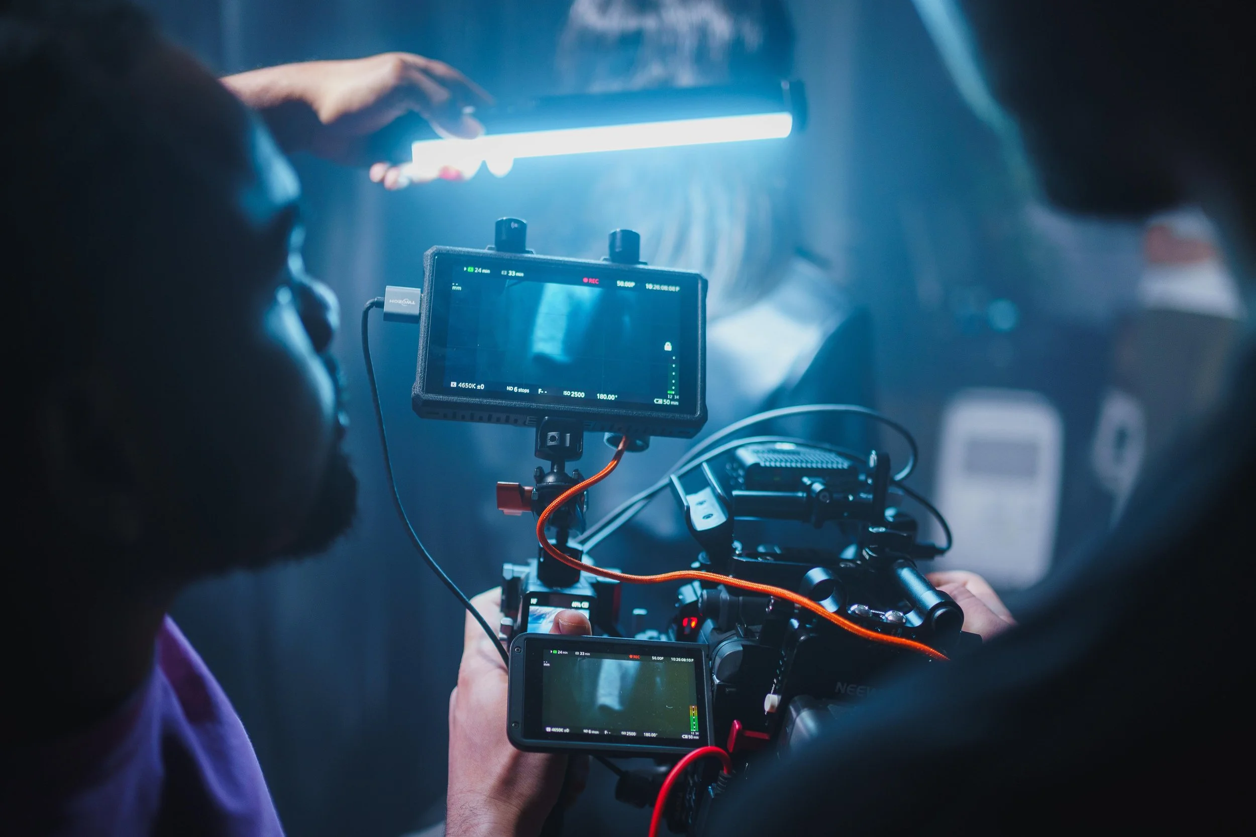 Two filmmakers set up a camera and lighting equipment for a shoot in a dimly lit space.