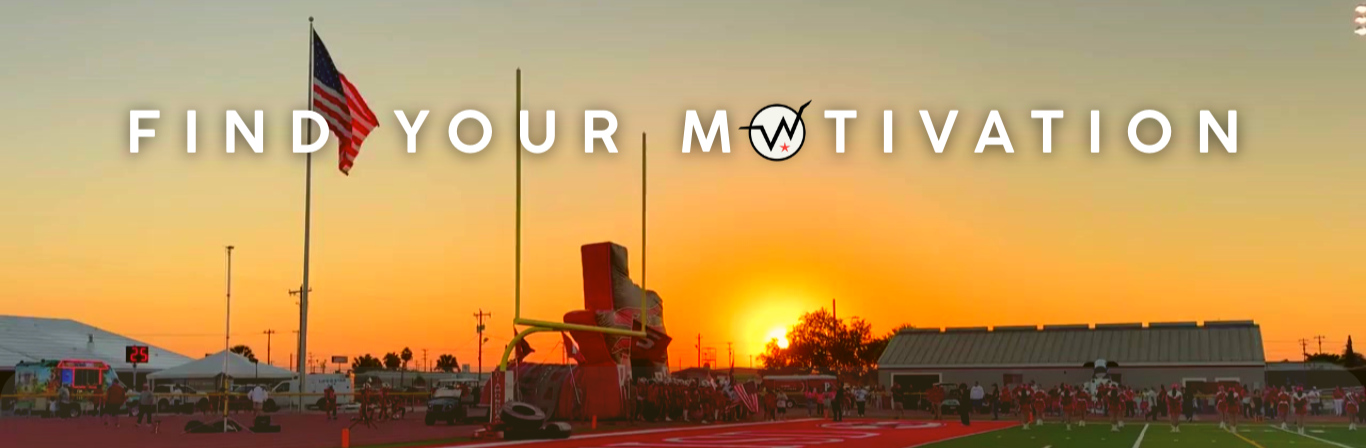 A fireworks display at a sports stadium during sunset, with a crowd gathered, American flags, and a large inflatable football figure.