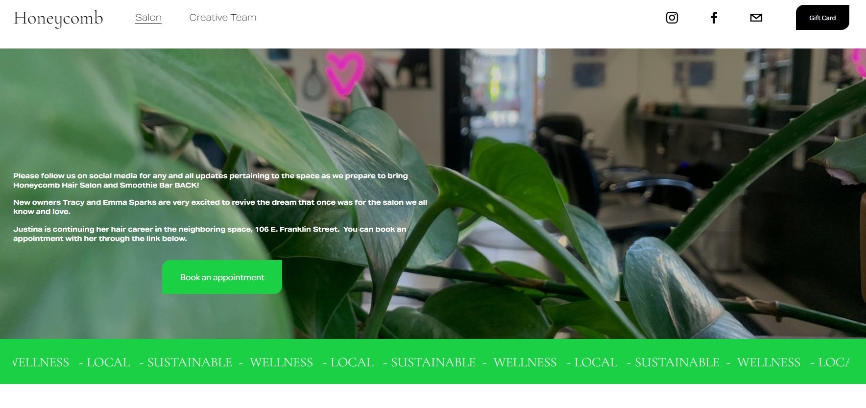 Plant interior with green leaves and pink neon heart decoration, interior of a salon visible in the background.