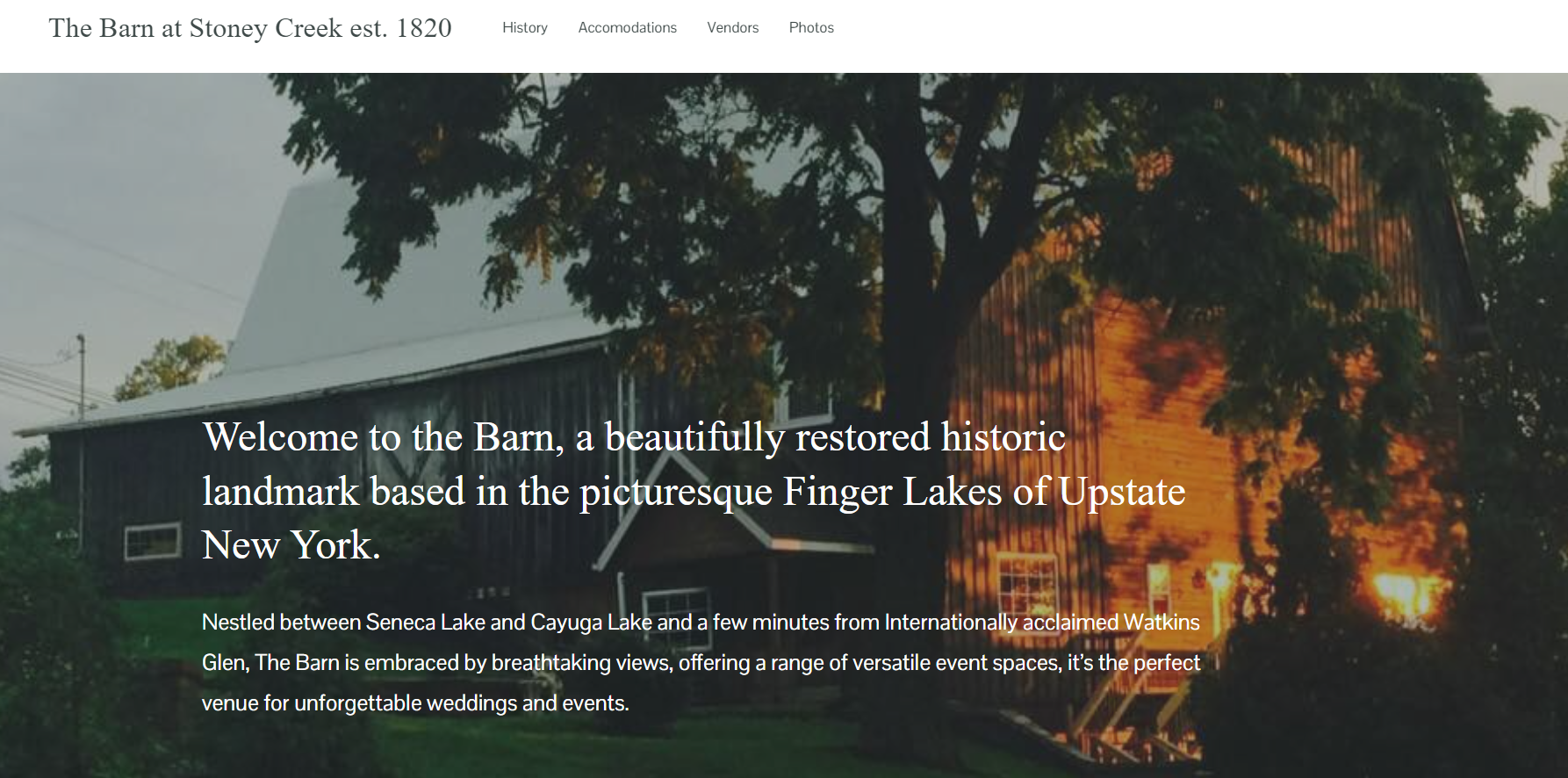 Photo of a historic barn with a tree in front, nestled between lakes in Upstate New York, with sunlight casting a glow on the wooden exterior.