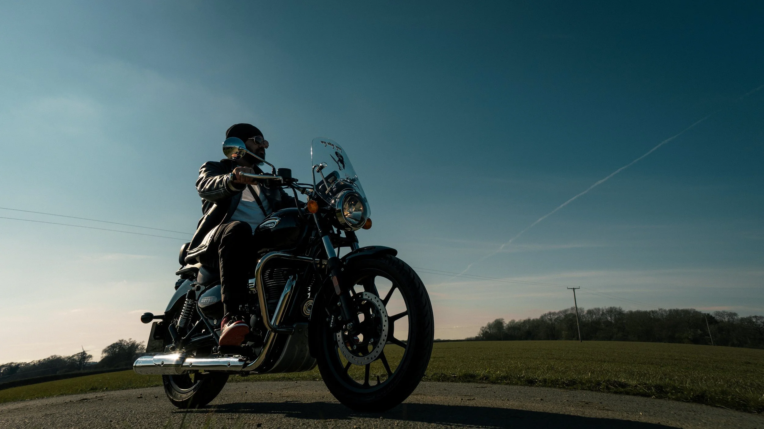 Person riding a black motorcycle on a rural road during sunset.