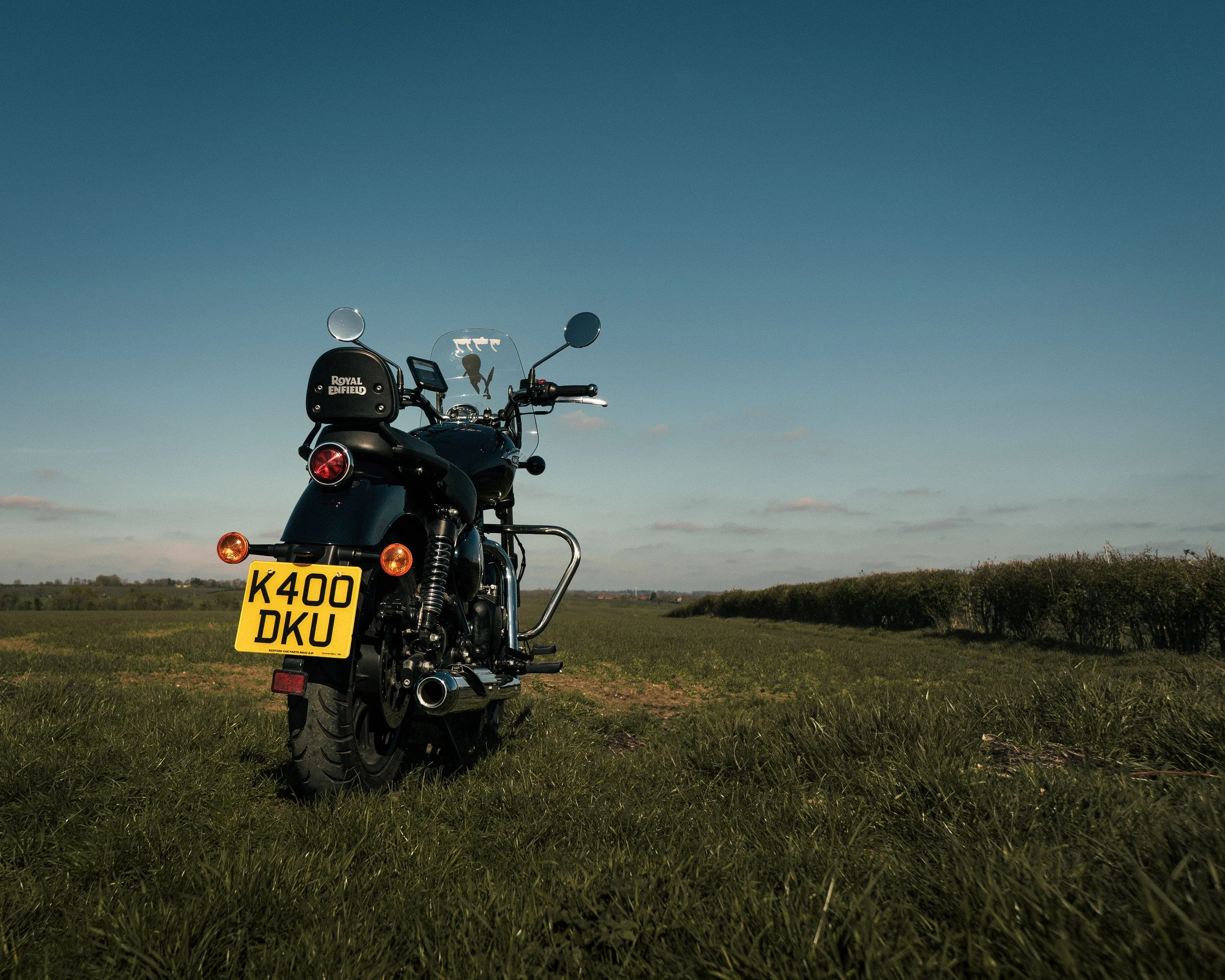 Black motorcycle with UK license plate K400 DKU parked on a grassy field under a blue sky with sparse clouds.
