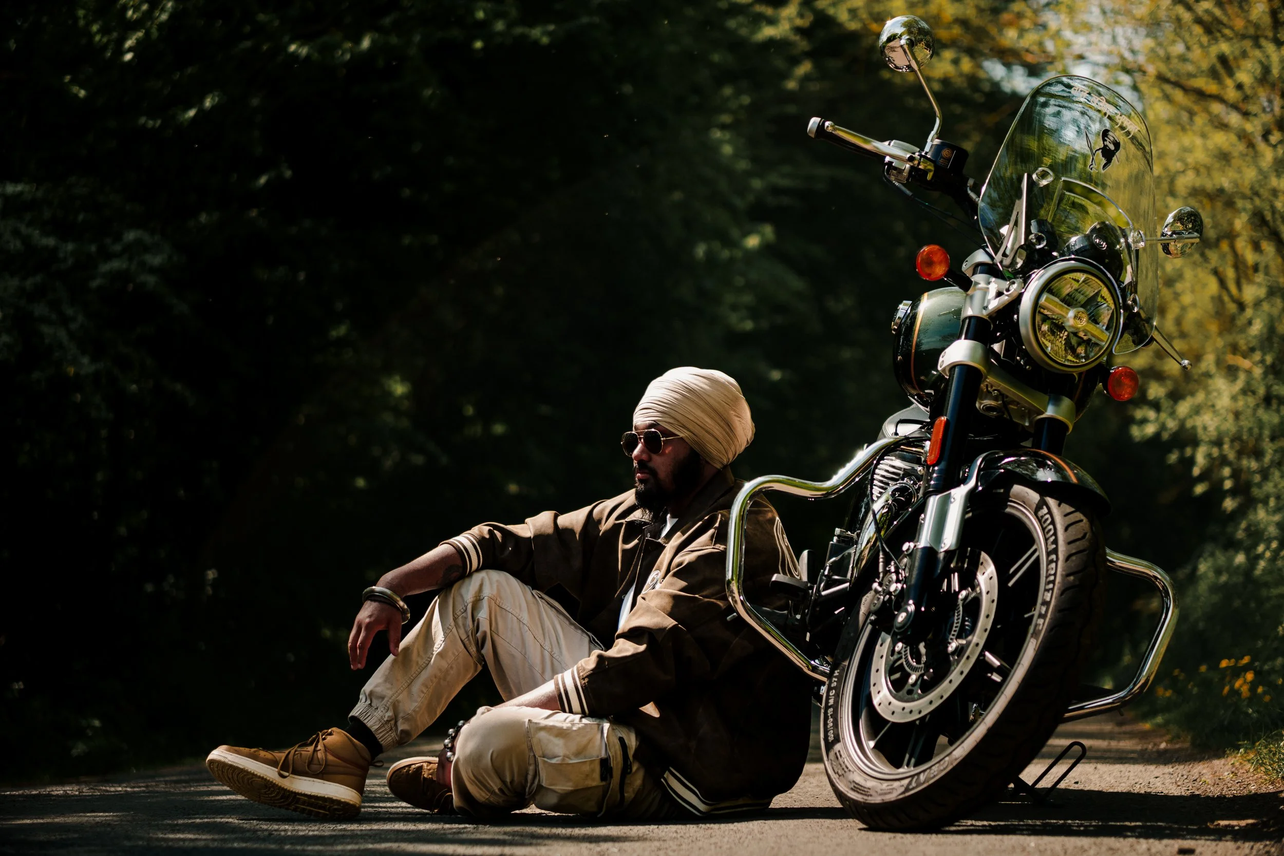 A man sitting on the ground next to a motorcycle in a wooded area.