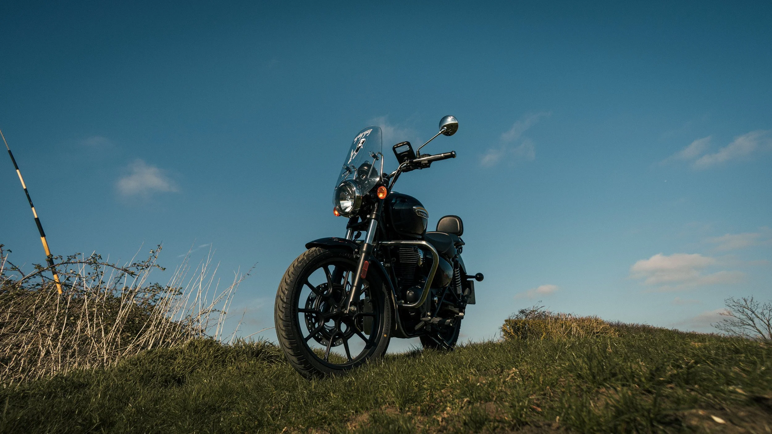 A black motorcycle parked on a grassy hill with a clear blue sky in the background.