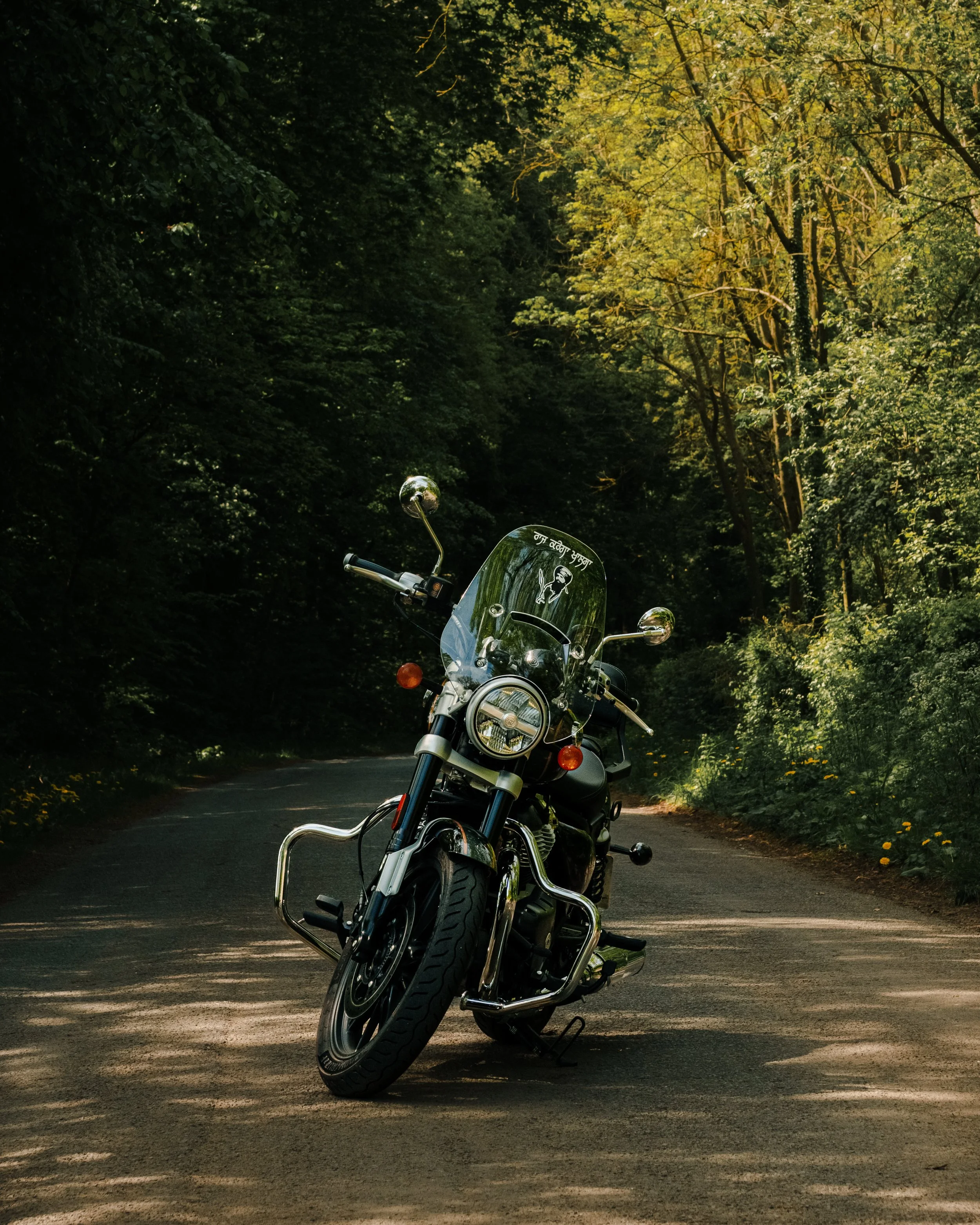 A black motorcycle parked on a winding forest road surrounded by green trees and sunlight.