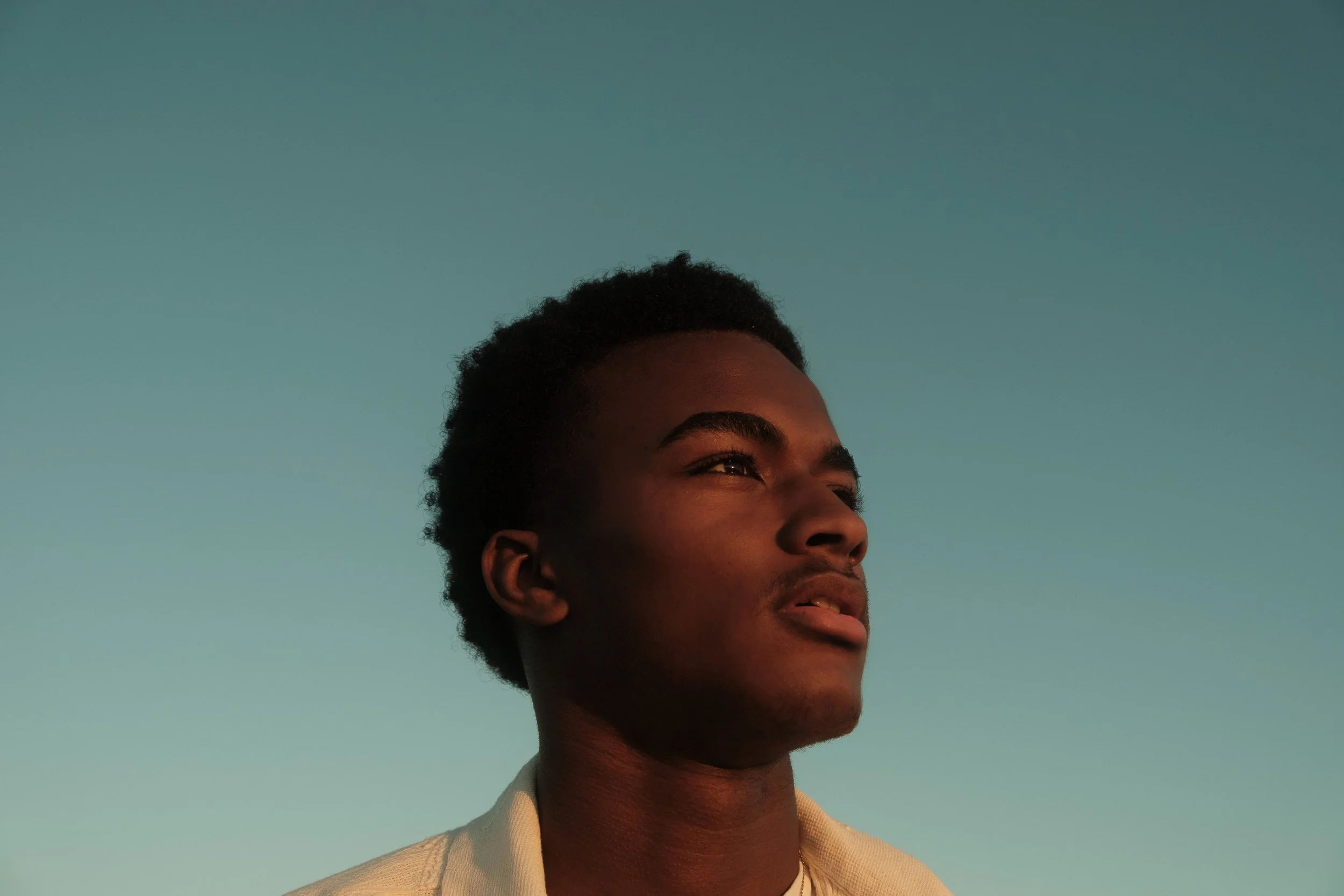 Lucas Ortet, Portuguese musician and song writer gazing into the distance against a clear blue sky.