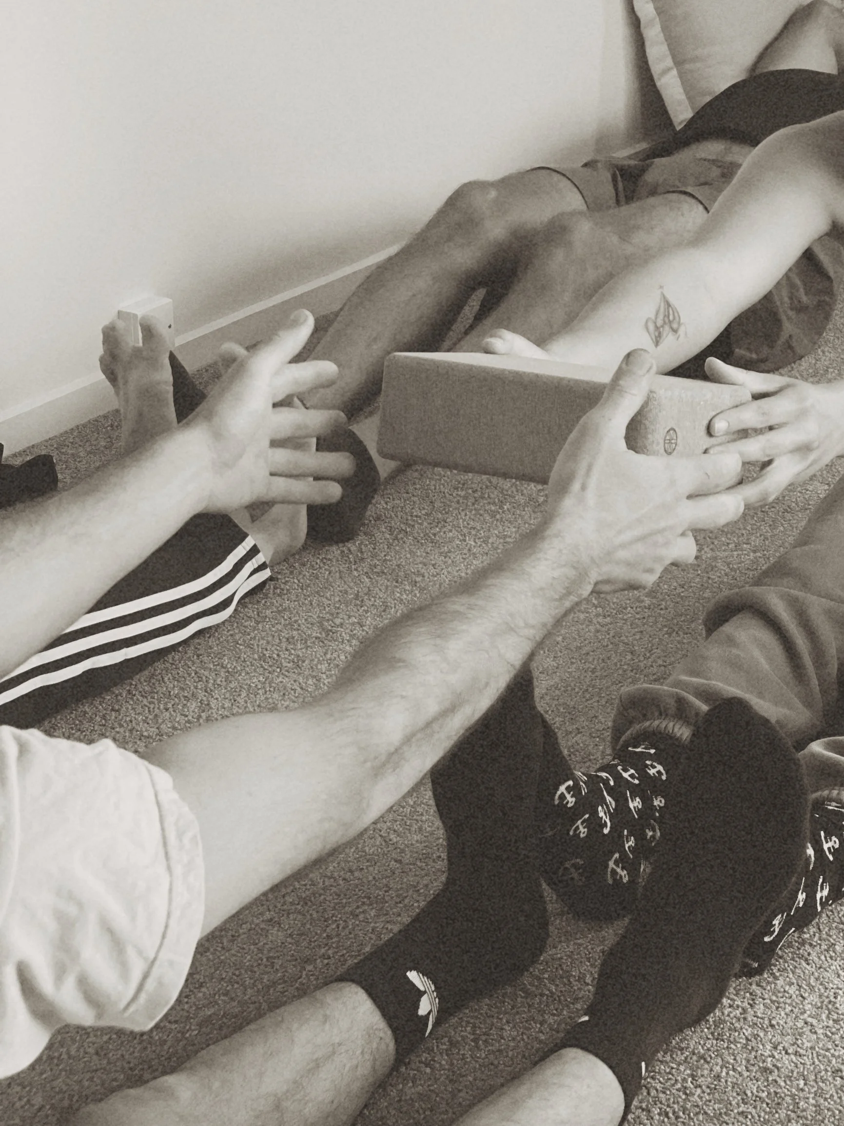 Two people engaging in a core-strengthening partner exercise, passing a yoga block between them to build strength, stability, and teamwork.