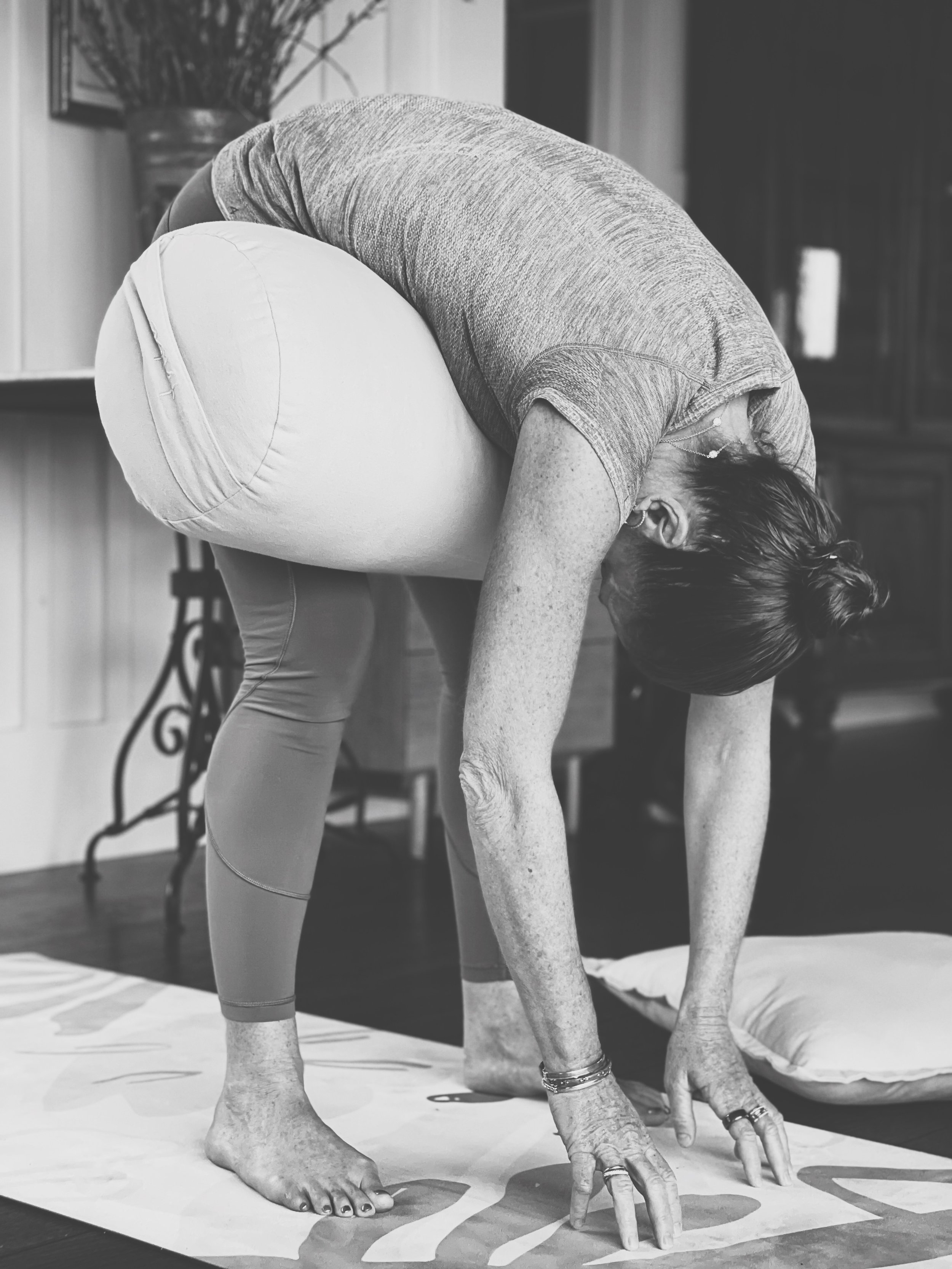 Person in a yoga pose with bolster for support on a mat indoors.