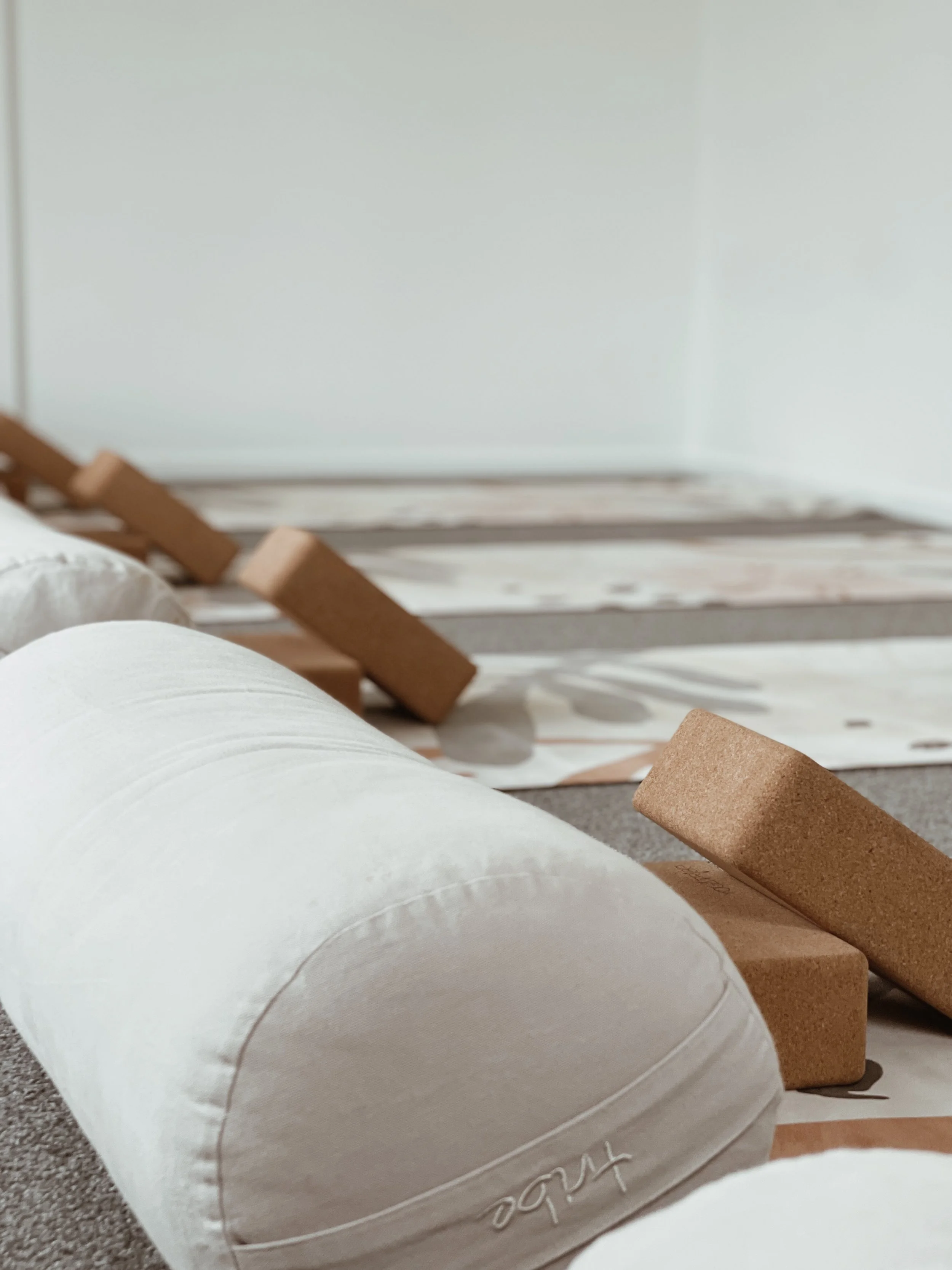 Yoga studio with white bolsters, cork blocks, and yoga mats on a carpeted floor.