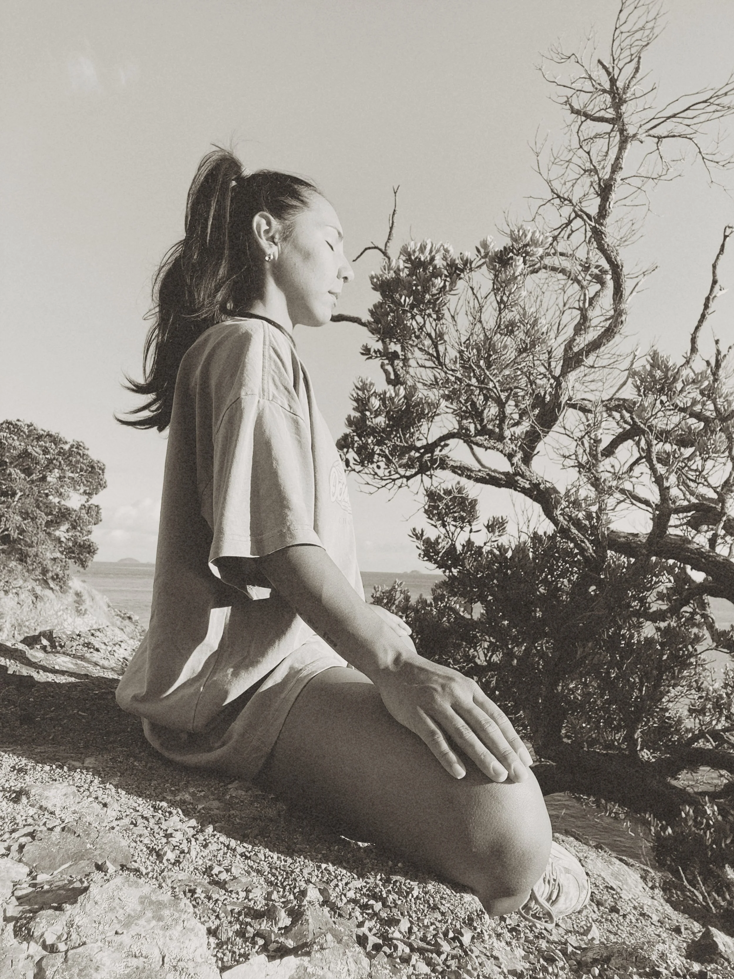 Woman meditating outdoors on rocky terrain with trees in background