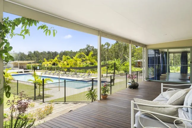 View from a screened porch overlooking a backyard with a swimming pool, lounge chairs, and lush green trees.