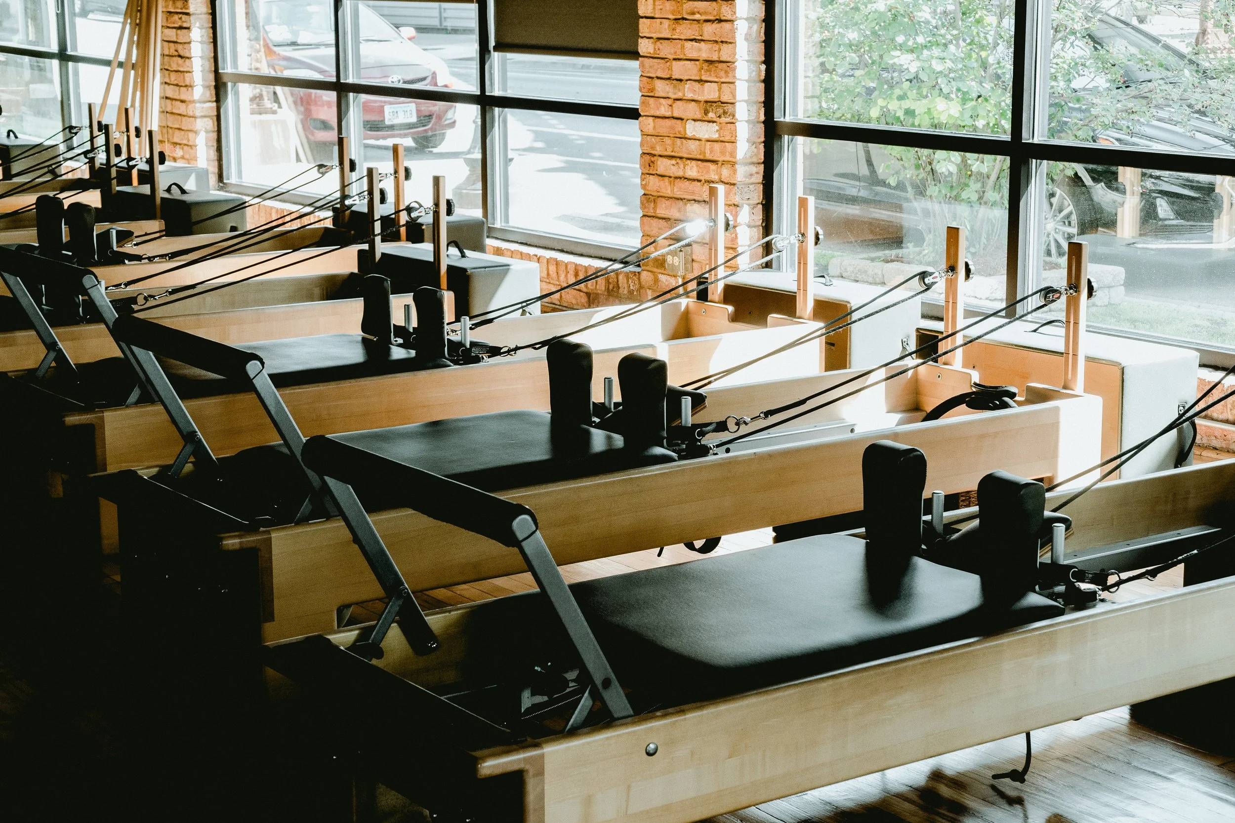 Row of Pilates reformer machines in a fitness studio with large windows and brick walls.