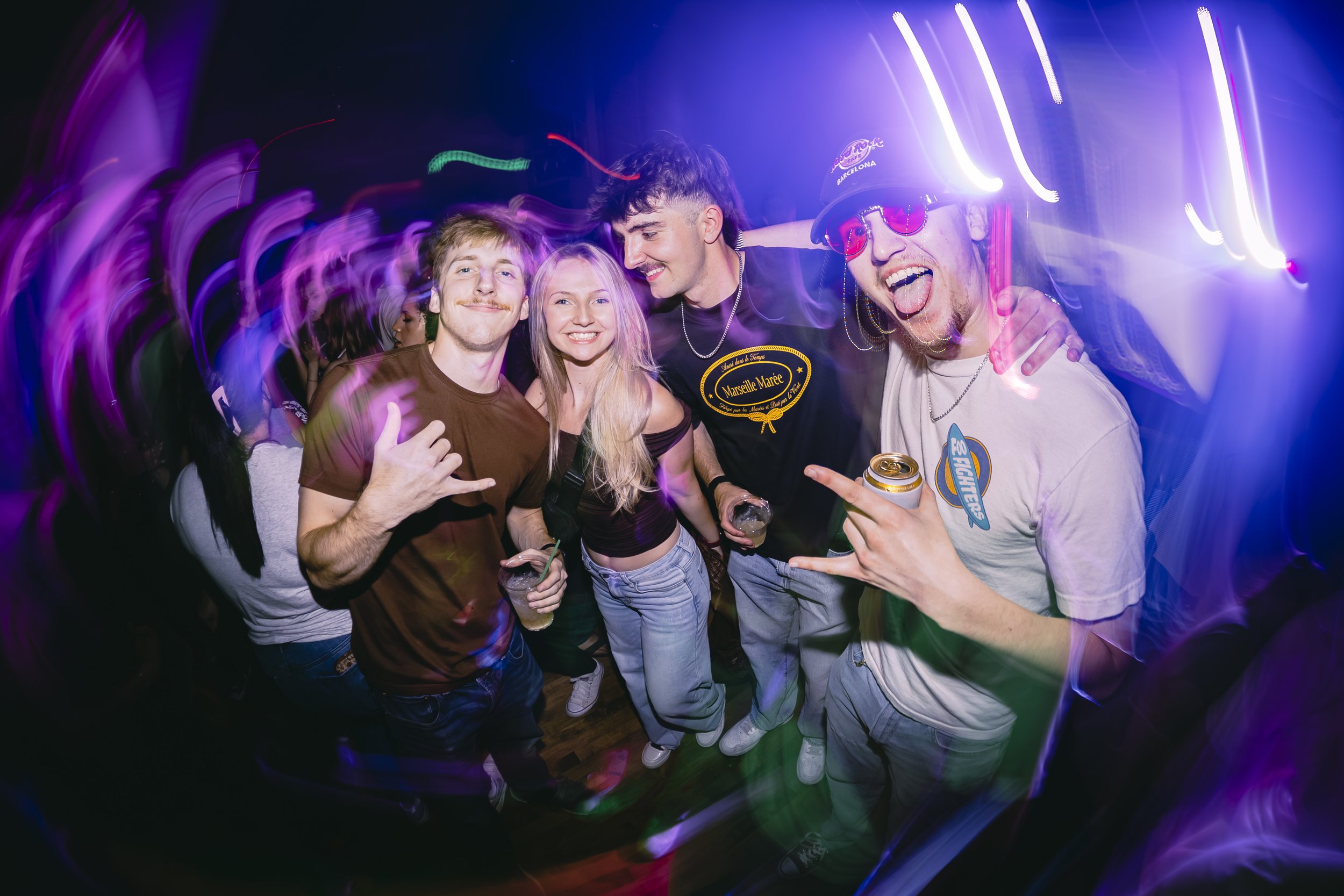 Four young friends at a nightclub enjoying themselves, surrounded by colorful lights and dancing.