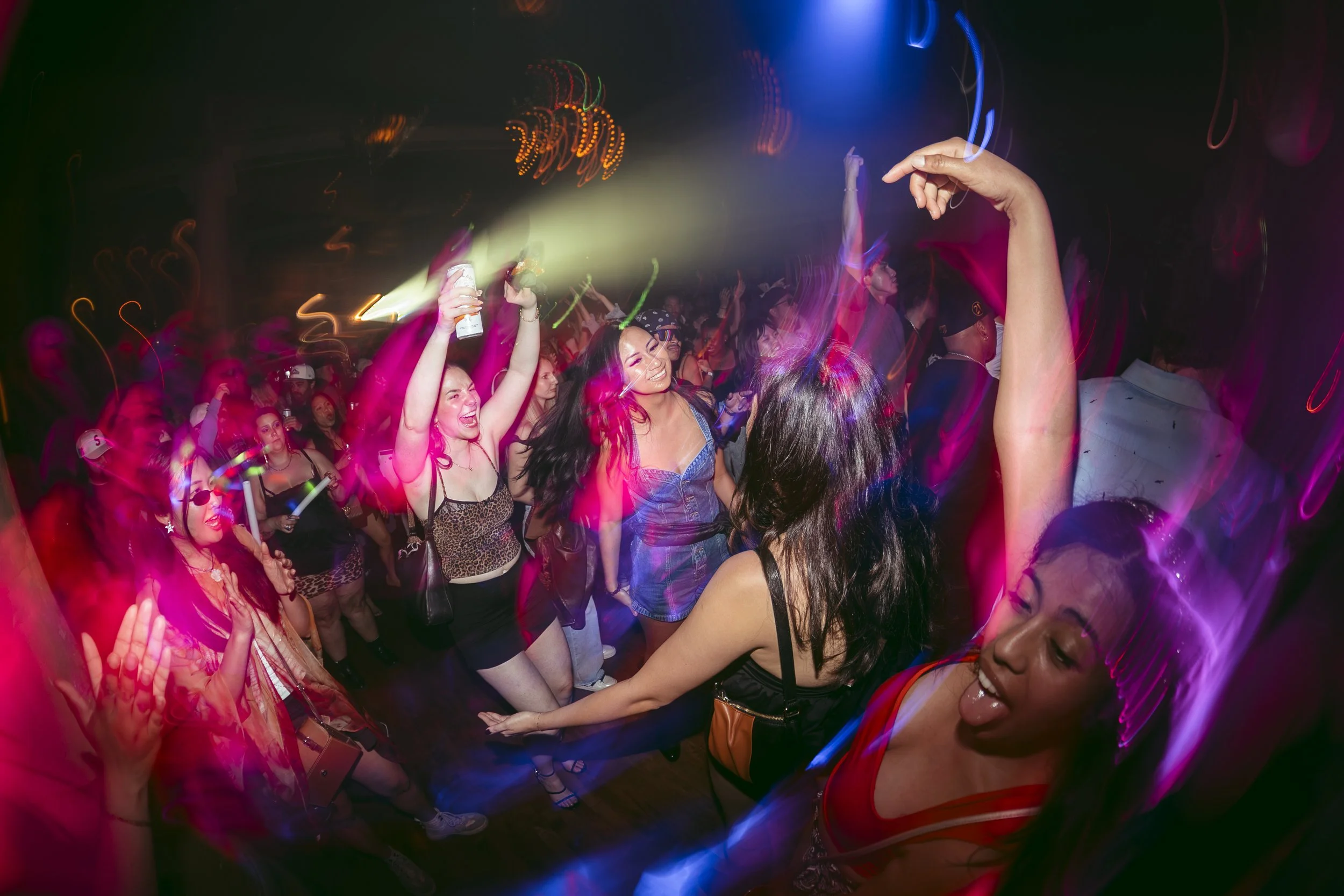 People dancing and enjoying a party with colorful lights and some holding drinks.